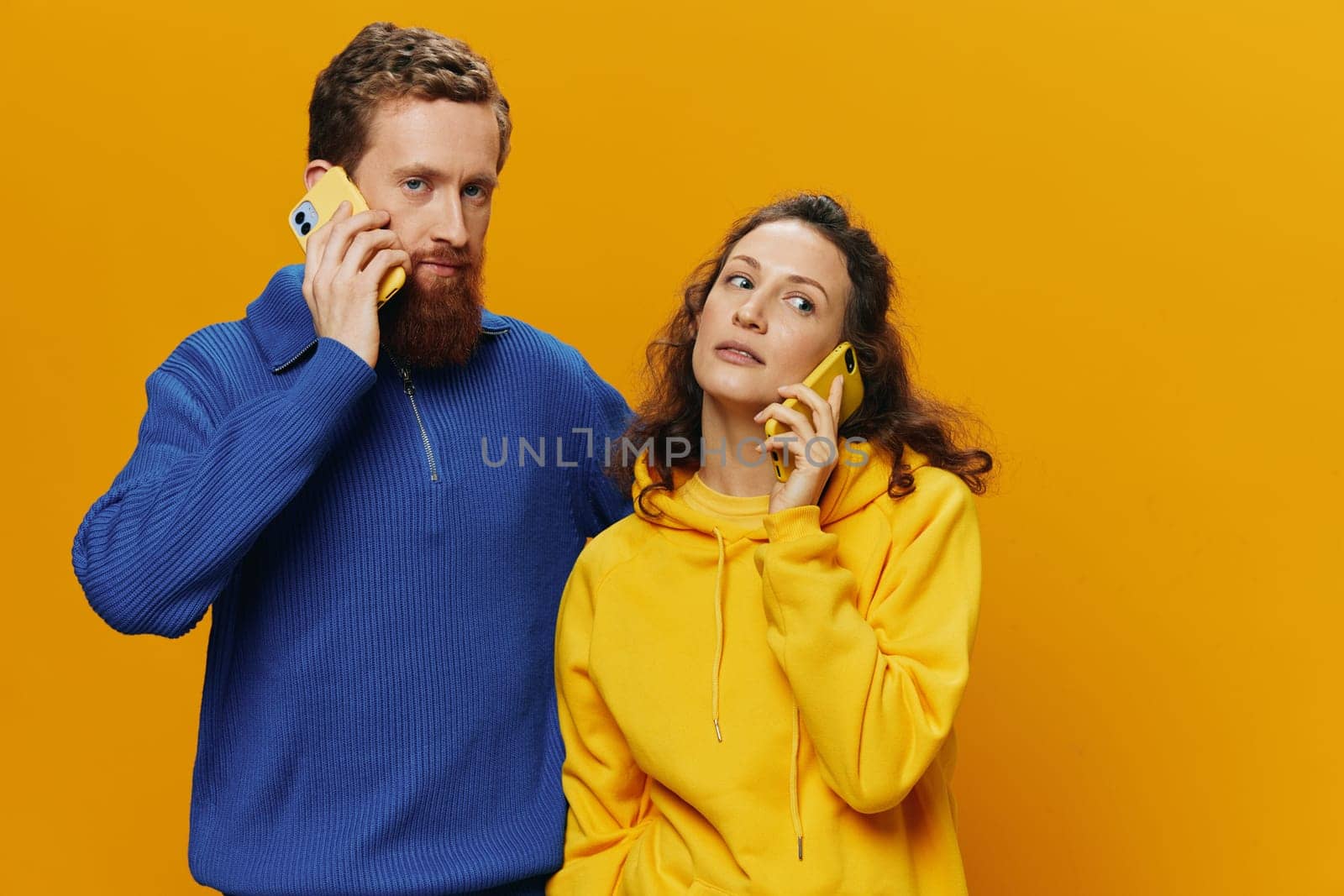 Man and woman couple smiling merrily with phone in hand social media viewing photos and videos, on yellow background, symbols signs and hand gestures, family freelancers. High quality photo