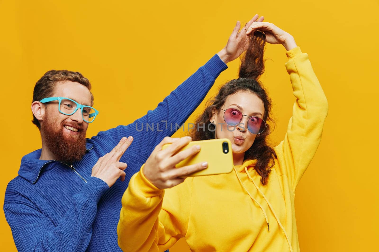 Woman and man funny couple with phones in hand social networking and communication crooked do selfies smile fun, on yellow background. The concept of real family relationships, freelancers, work online. High quality photo