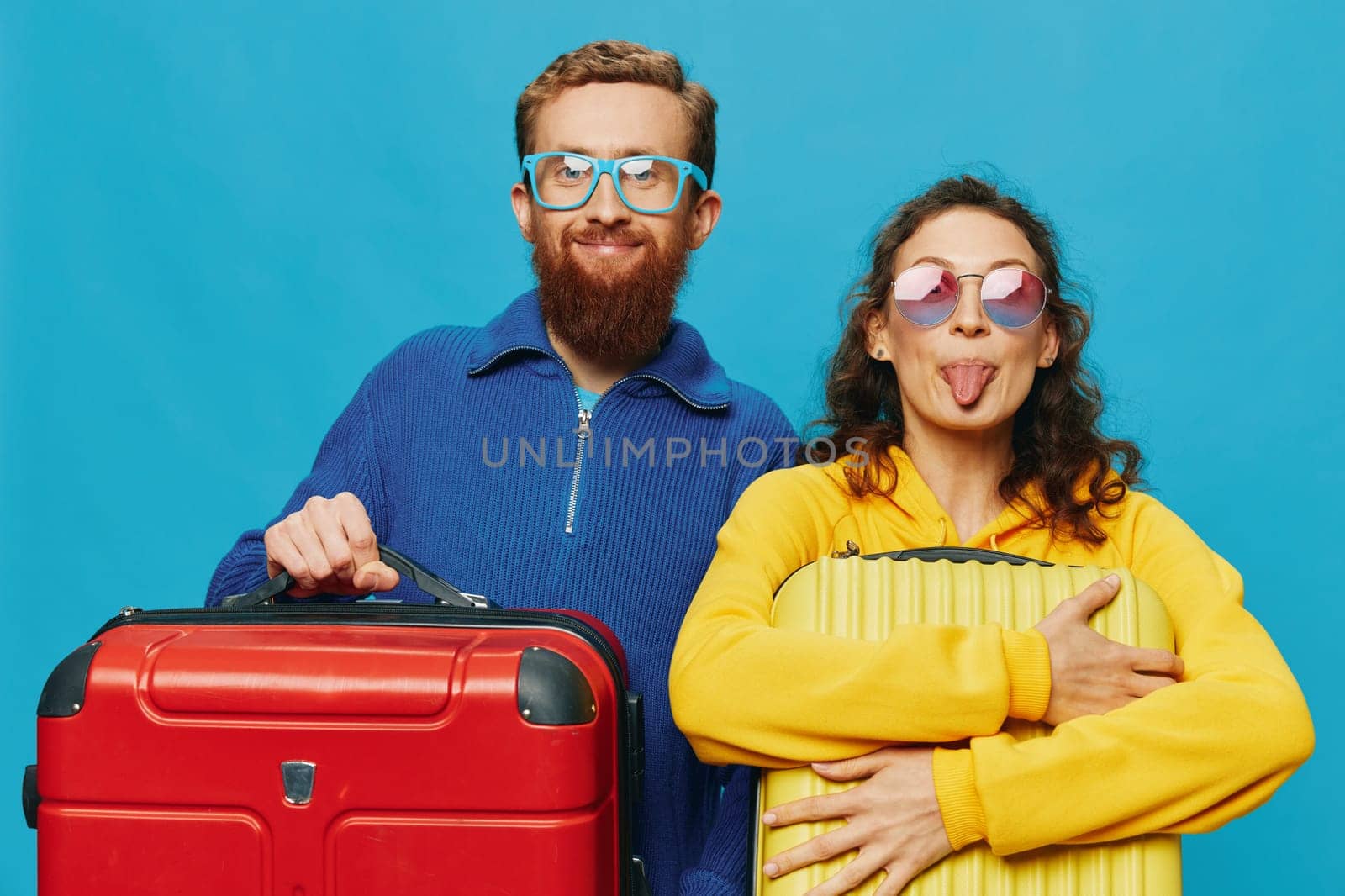 Woman and man smile suitcases in hand with yellow and red suitcase smile fun, on blue background, packing for a trip, family vacation trip. High quality photo