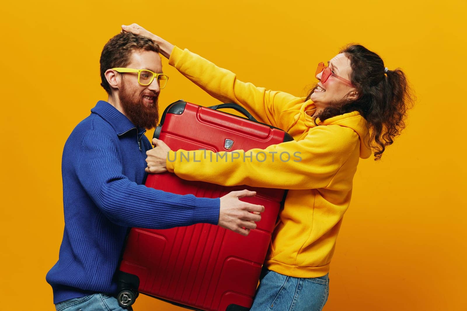 Woman and man smiling, suitcases in hand with yellow and red suitcase smiling merrily and crooked, yellow background, going on a trip, family vacation trip, newlyweds. by SHOTPRIME