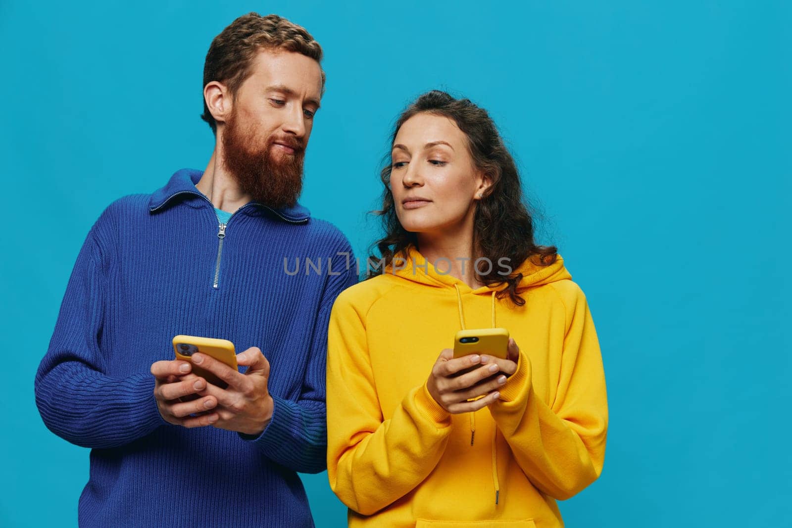 Woman and man cheerful couple with phones in their hands crooked smile cheerful, on blue background. The concept of real family relationships, talking on the phone, work online. by SHOTPRIME