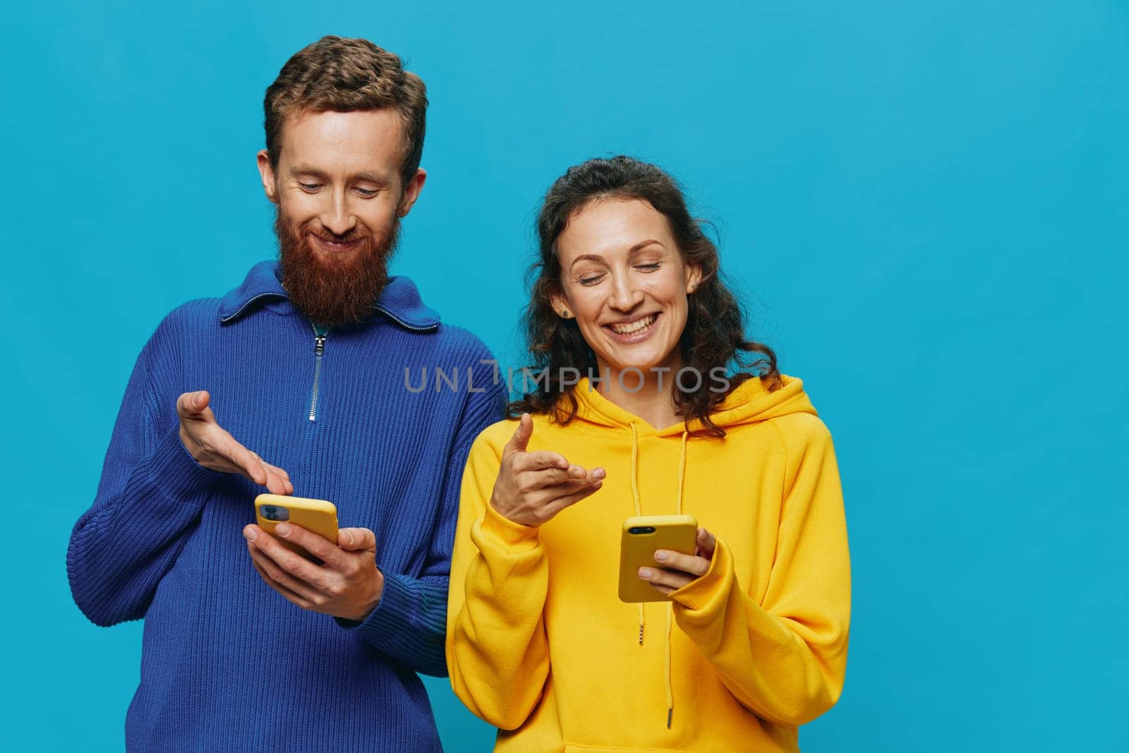 Woman and man cheerful couple with phones in their hands crooked smile cheerful, on blue background. The concept of real family relationships, talking on the phone, work online. by SHOTPRIME