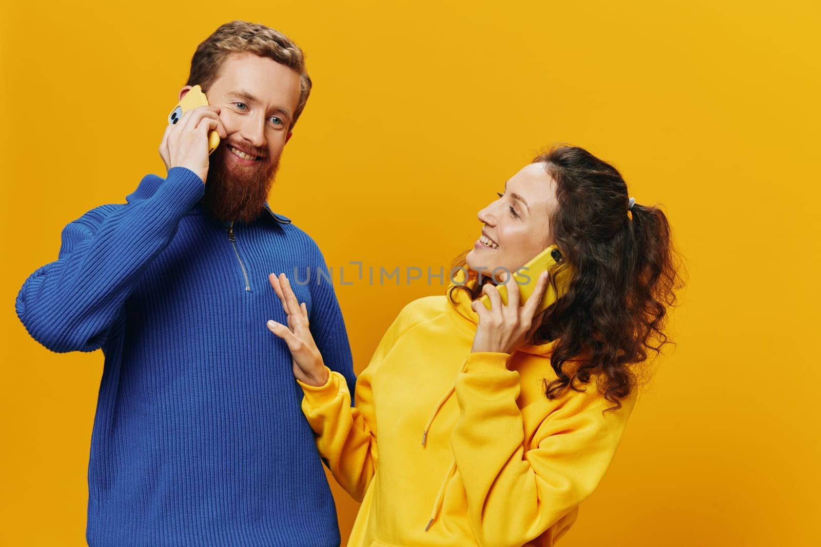 Woman and man cheerful couple with phones in hand talking on cell phone crooked smile cheerful, on yellow background. The concept of real family relationships, talking on the phone, work online. High quality photo