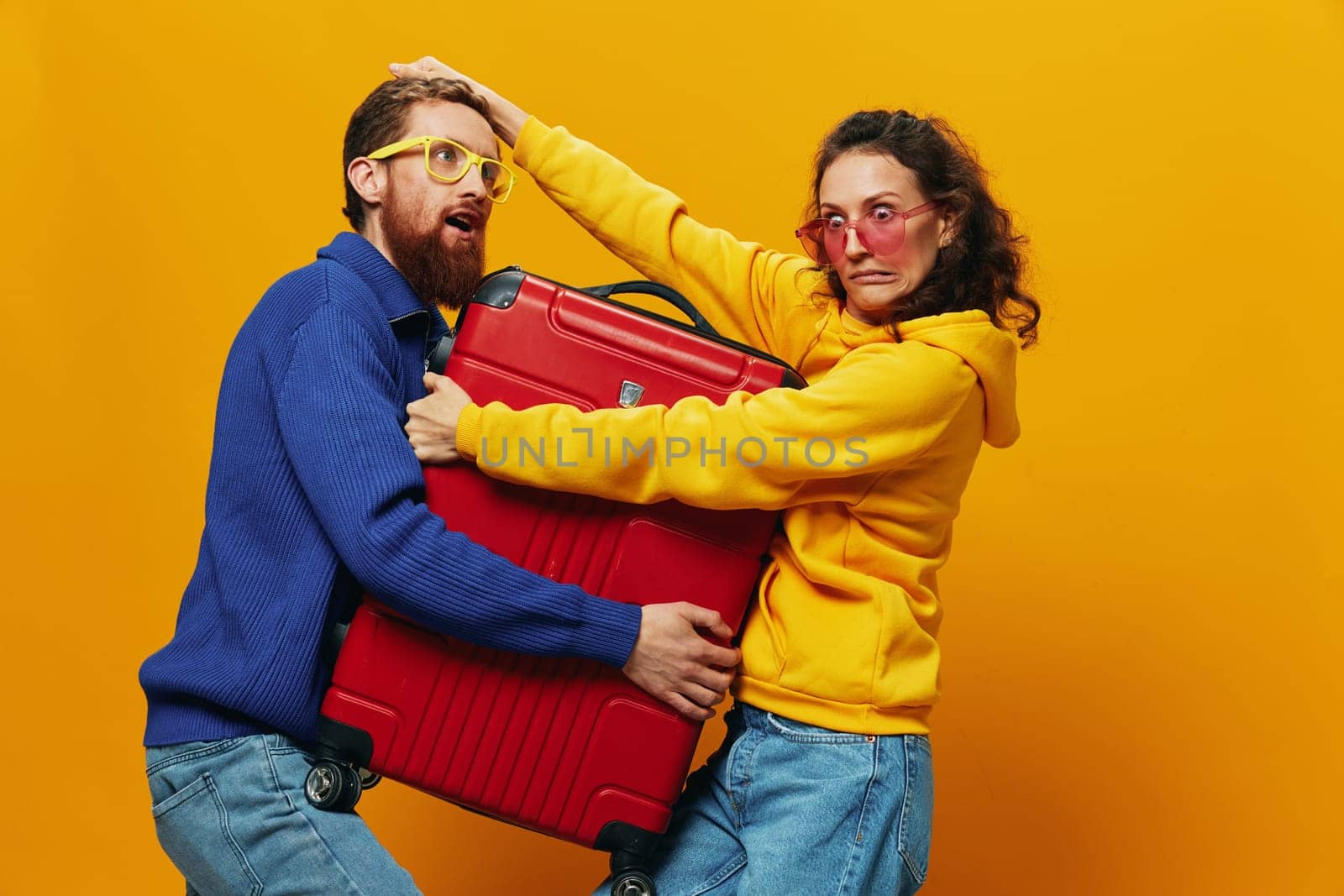 Woman and man smiling, suitcases in hand with yellow and red suitcase smiling merrily and crooked, yellow background, going on a trip, family vacation trip, newlyweds. by SHOTPRIME