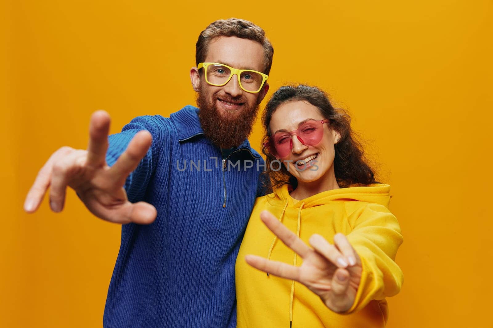Man and woman couple smiling cheerfully and crooked with glasses, on yellow background, symbols signs and hand gestures, family shoot, newlyweds. by SHOTPRIME