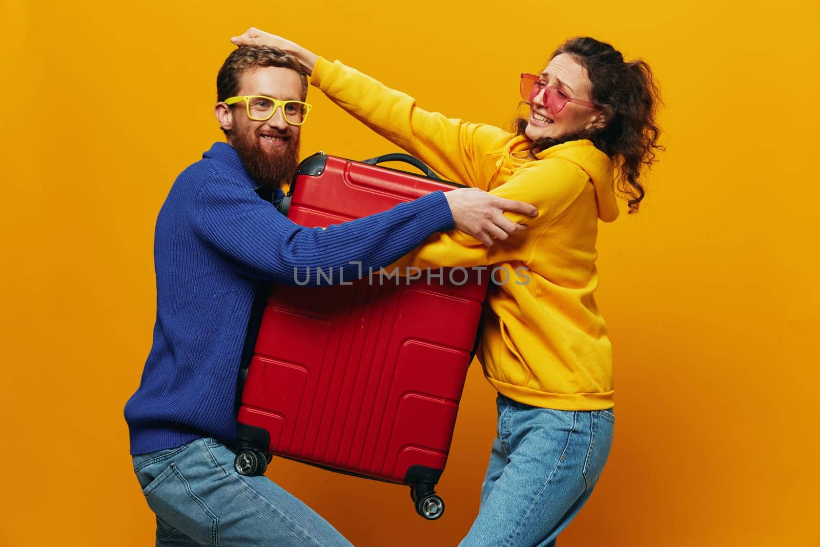 Woman and man smiling, suitcases in hand with yellow and red suitcase smiling merrily and crooked, yellow background, going on a trip, family vacation trip, newlyweds. by SHOTPRIME