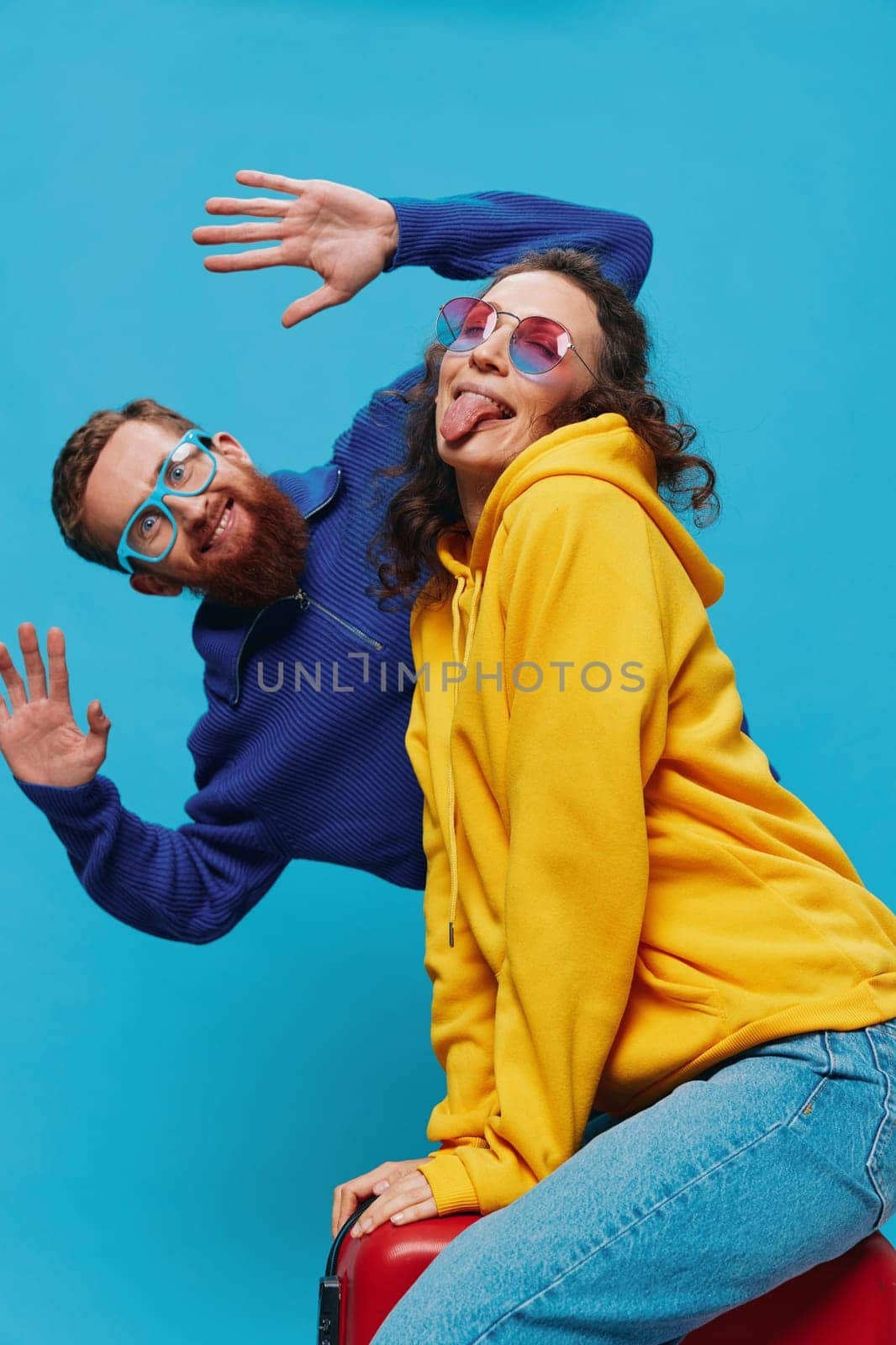 Woman and man smile sitting on suitcase with red suitcase smile, on blue background, packing for trip, family vacation trip. High quality photo