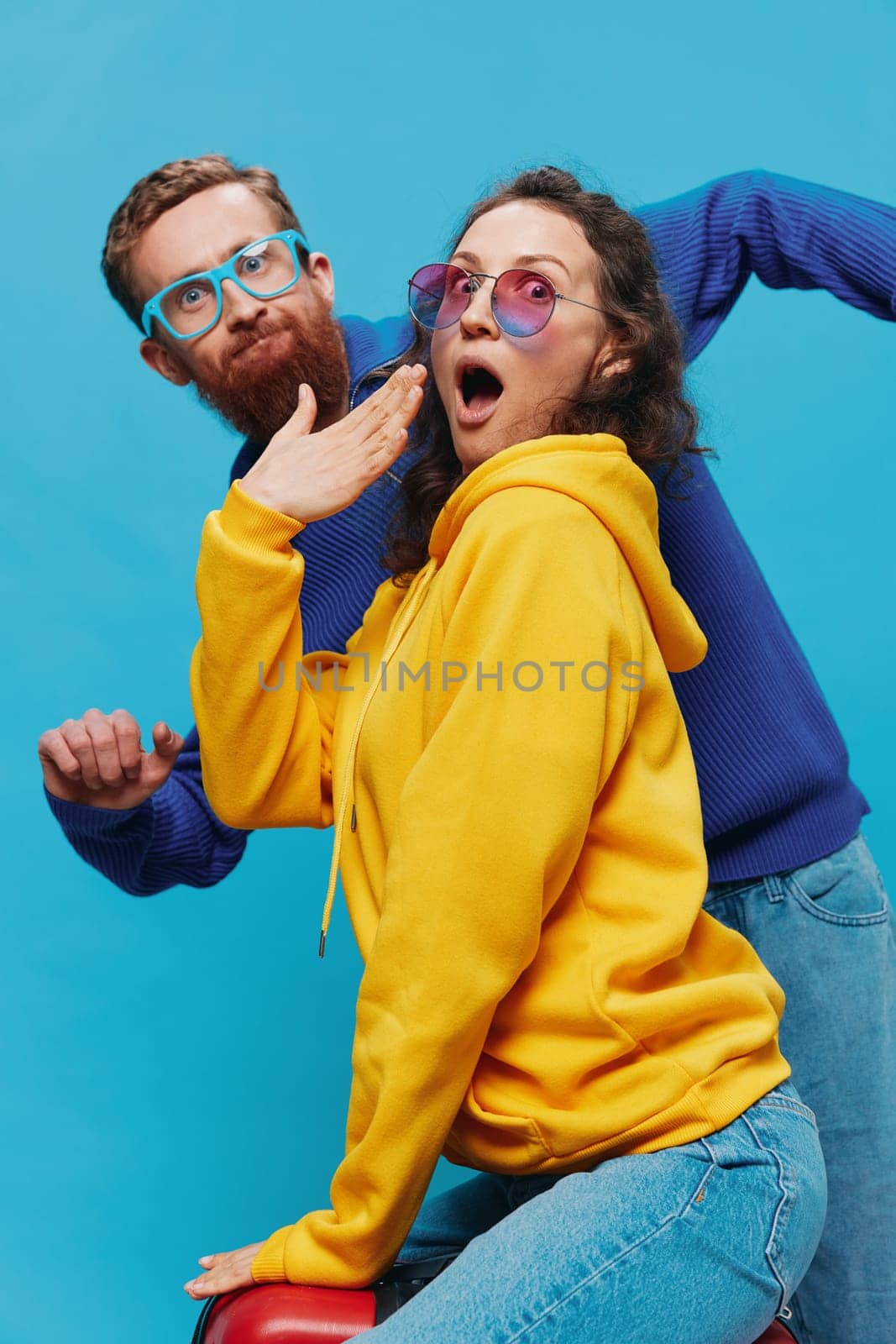 Woman and man smile sitting on suitcase with red suitcase smile, on blue background, packing for trip, family vacation trip. by SHOTPRIME