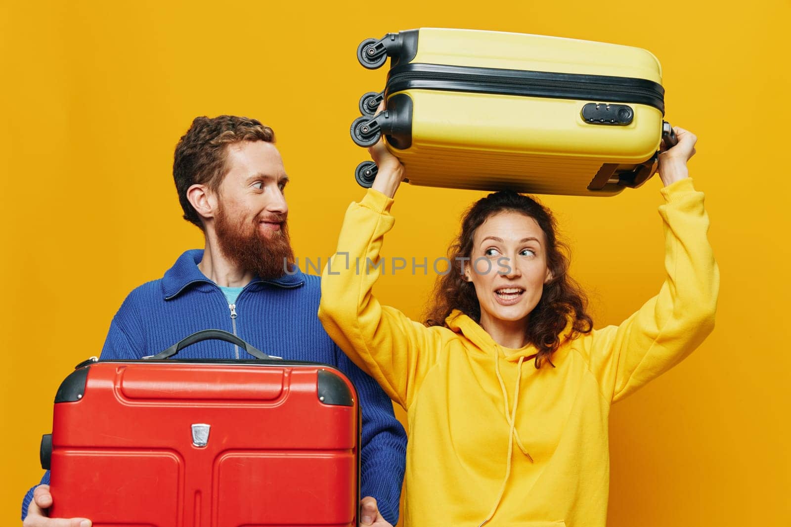 Woman and man smiling, suitcases in hand with yellow and red suitcase smiling merrily and crooked, yellow background, going on a trip, family vacation trip, newlyweds. High quality photo