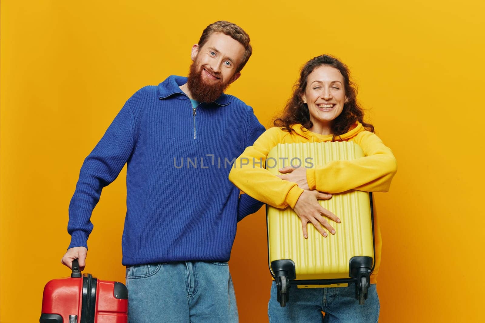 Woman and man smiling, suitcases in hand with yellow and red suitcase smiling merrily and crooked, yellow background, going on a trip, family vacation trip, newlyweds. High quality photo