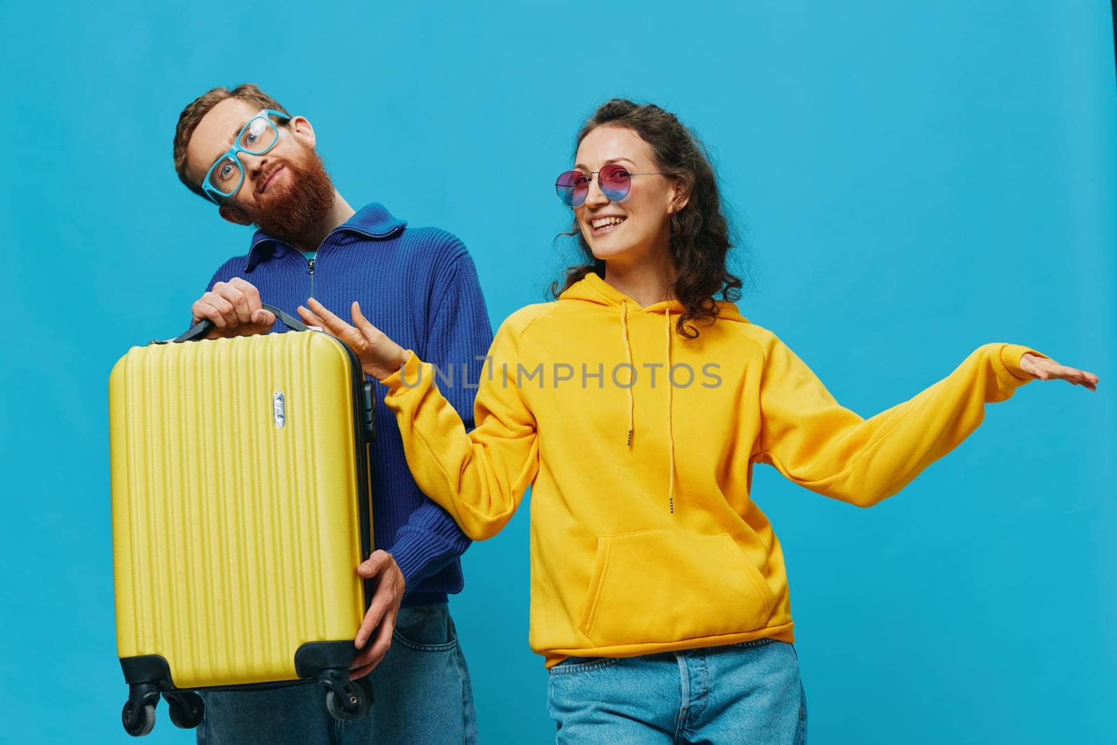 Woman and man smile sitting on suitcase with yellow suitcase smile, on blue background, packing for trip, family vacation trip. by SHOTPRIME