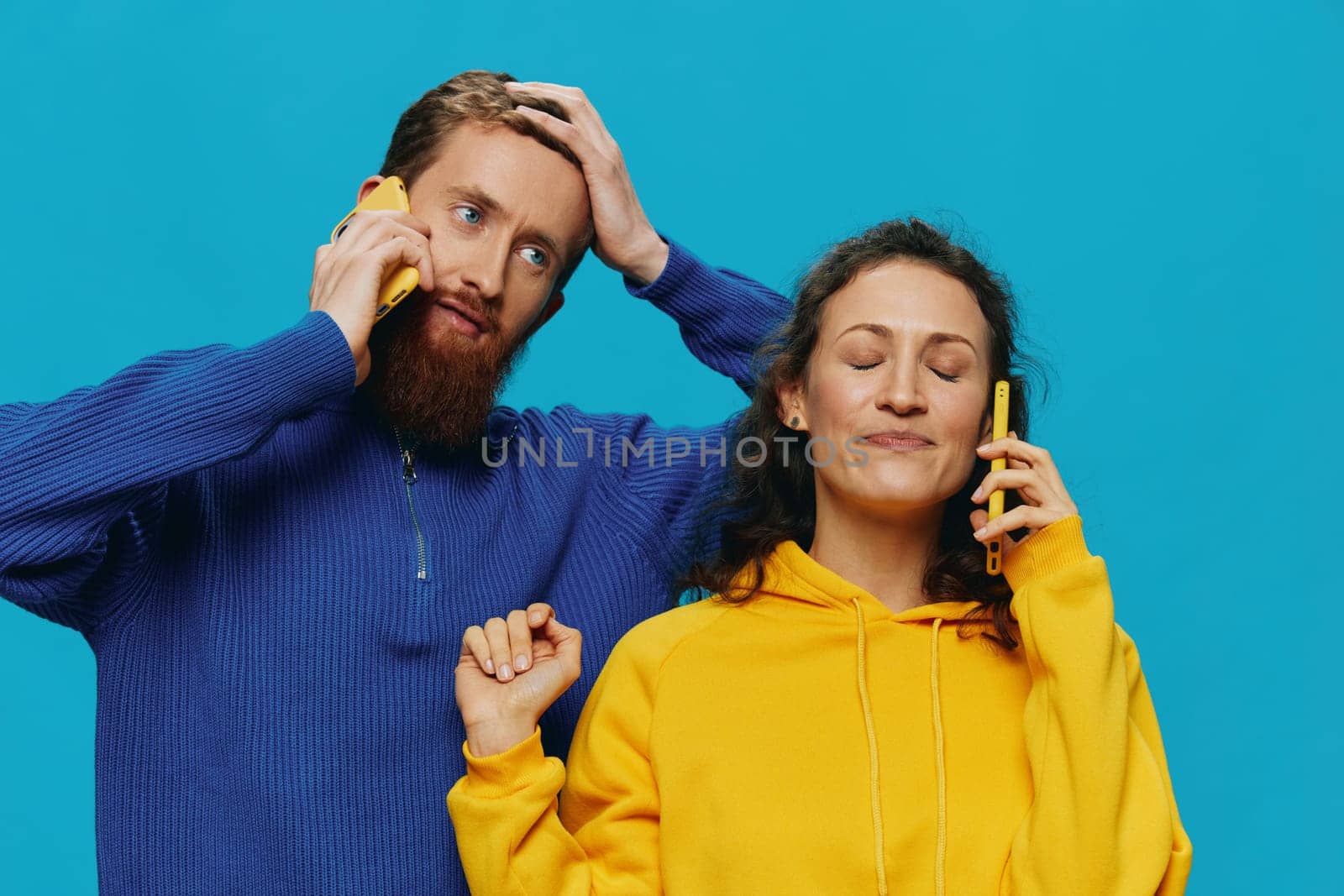 Woman and man cheerful couple with phones in their hands crooked smile cheerful, on blue background. The concept of real family relationships, talking on the phone, work online. High quality photo
