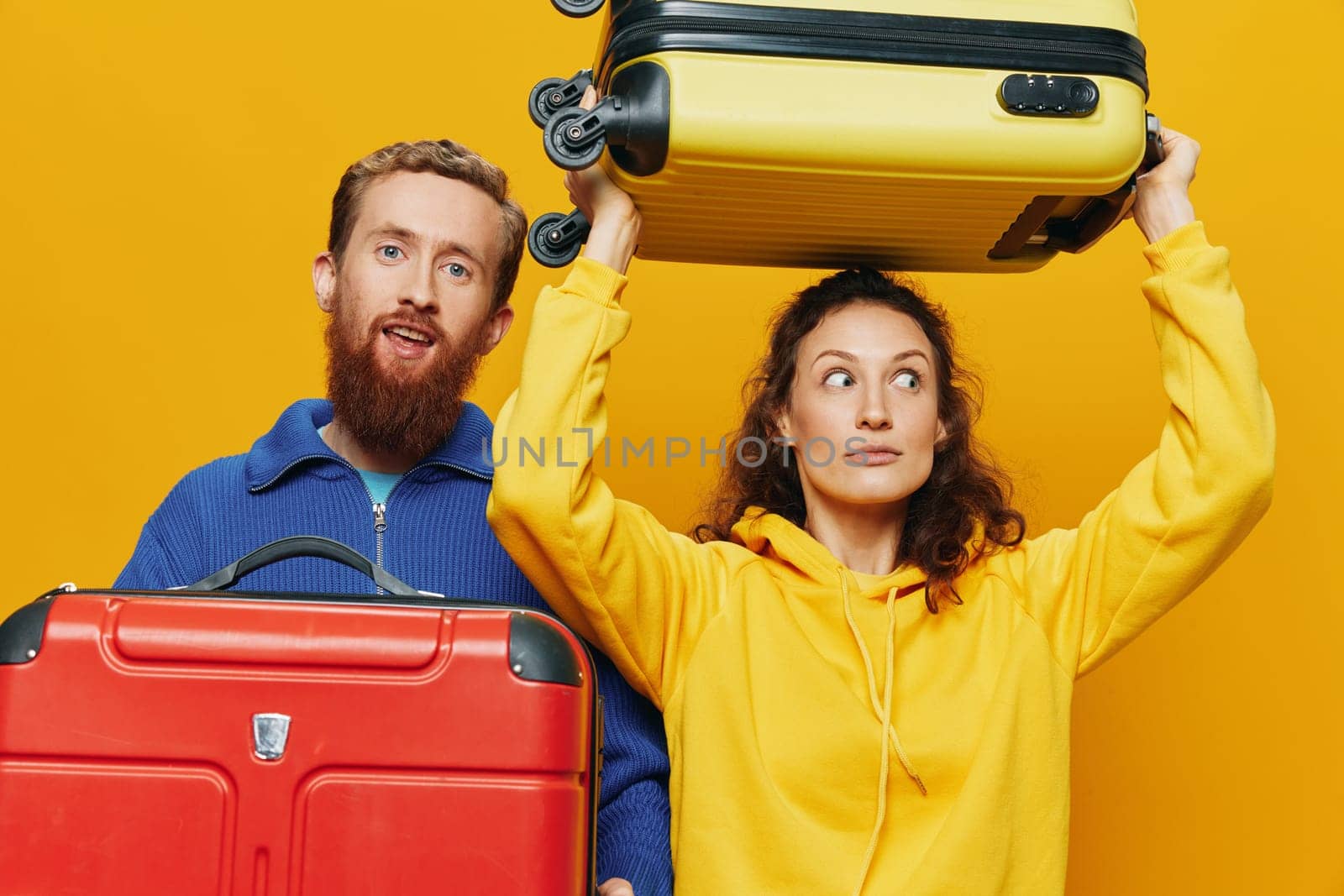 Woman and man smiling, suitcases in hand with yellow and red suitcase smiling merrily and crooked, yellow background, going on a trip, family vacation trip, newlyweds. High quality photo