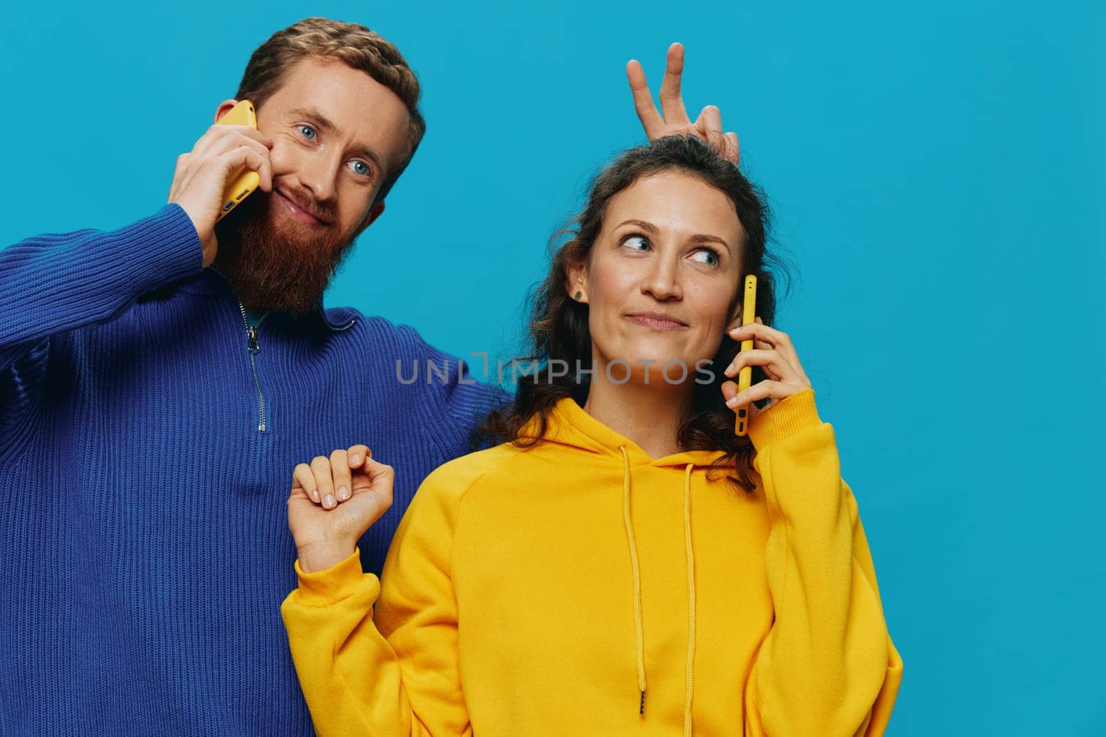 Woman and man cheerful couple with phones in their hands crooked smile cheerful, on blue background. The concept of real family relationships, talking on the phone, work online. by SHOTPRIME