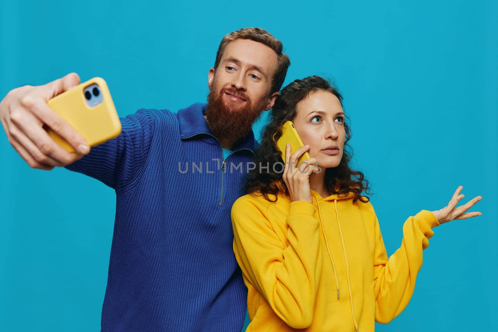 Woman and man funny couple with phones in hand taking selfies crooked smile fun, on blue background. The concept of real family relationships, talking on the phone, work online. by SHOTPRIME