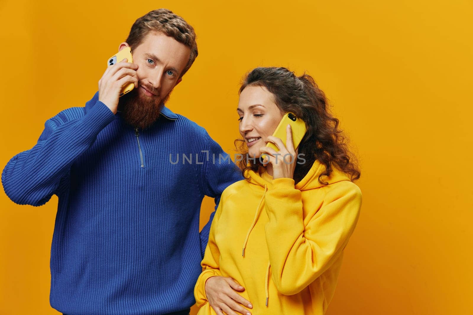 Man and woman couple smiling merrily with phone in hand social media viewing photos and videos, on yellow background, symbols signs and hand gestures, family freelancers. by SHOTPRIME
