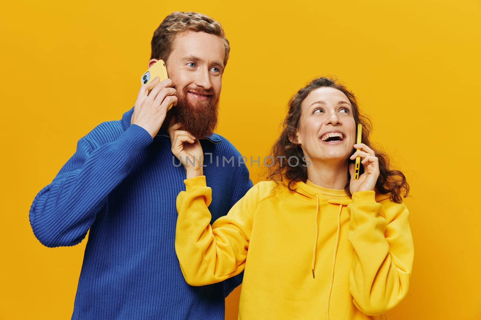 Woman and man cheerful couple with phones in hand talking on cell phone crooked smile cheerful, on yellow background. The concept of real family relationships, talking on the phone, work online. by SHOTPRIME