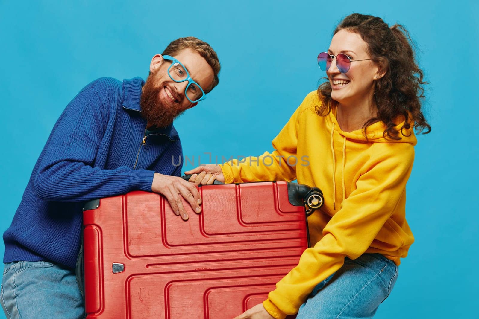 Woman and man smile suitcases in hand with yellow and red suitcase smile fun, on blue background, packing for a trip, family vacation trip. by SHOTPRIME