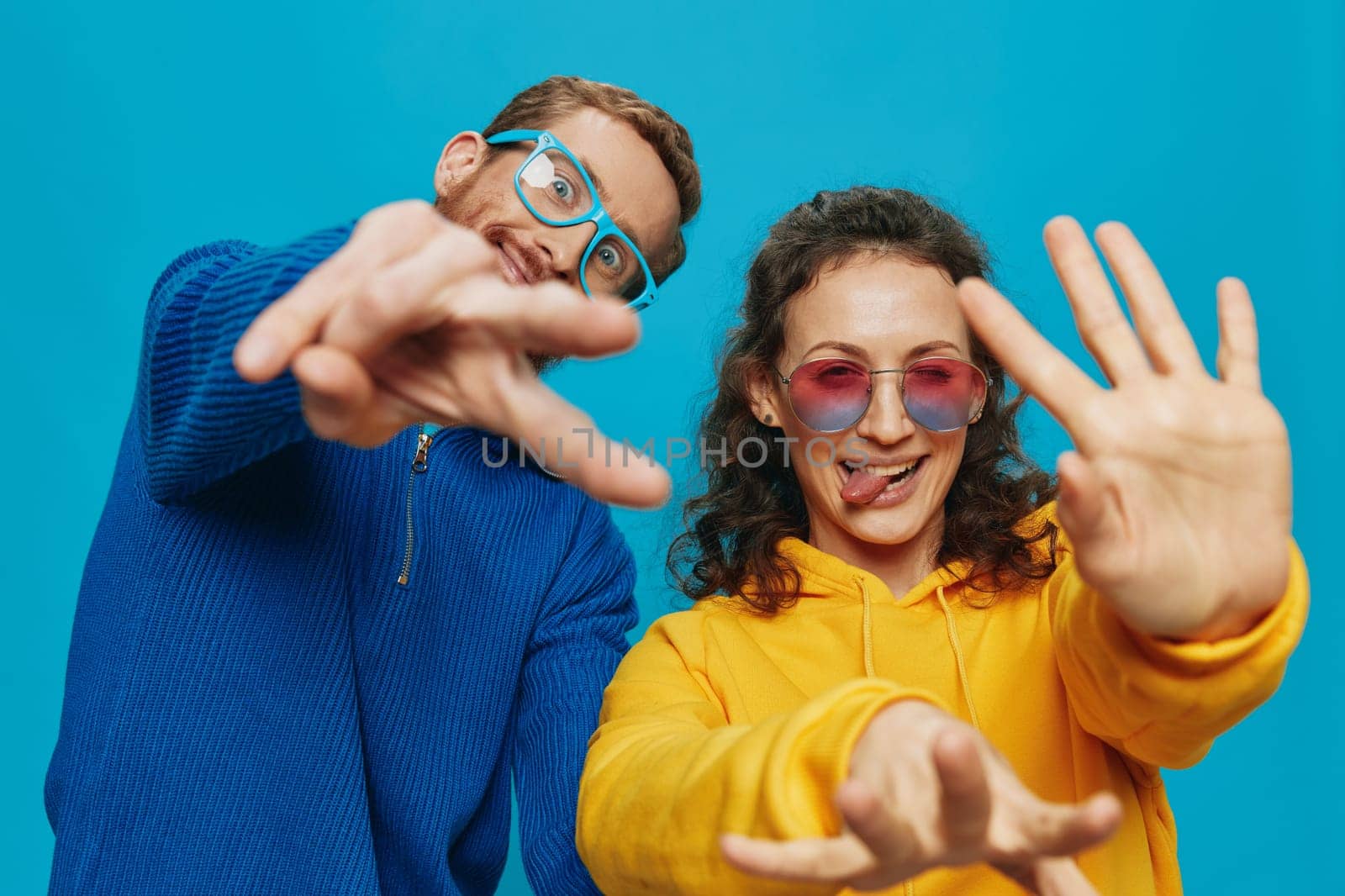 A woman and a man fun couple cranking and showing signs with their hands smiling cheerfully, on a blue background, The concept of a real relationship in a family. by SHOTPRIME