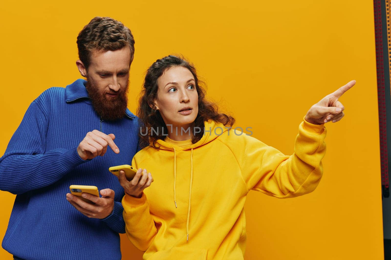 Woman and man cheerful couple with phones in hand social networking and communication crooked smile fun and fight, in yellow background. The concept of real family relationships, freelancers, work online. High quality photo