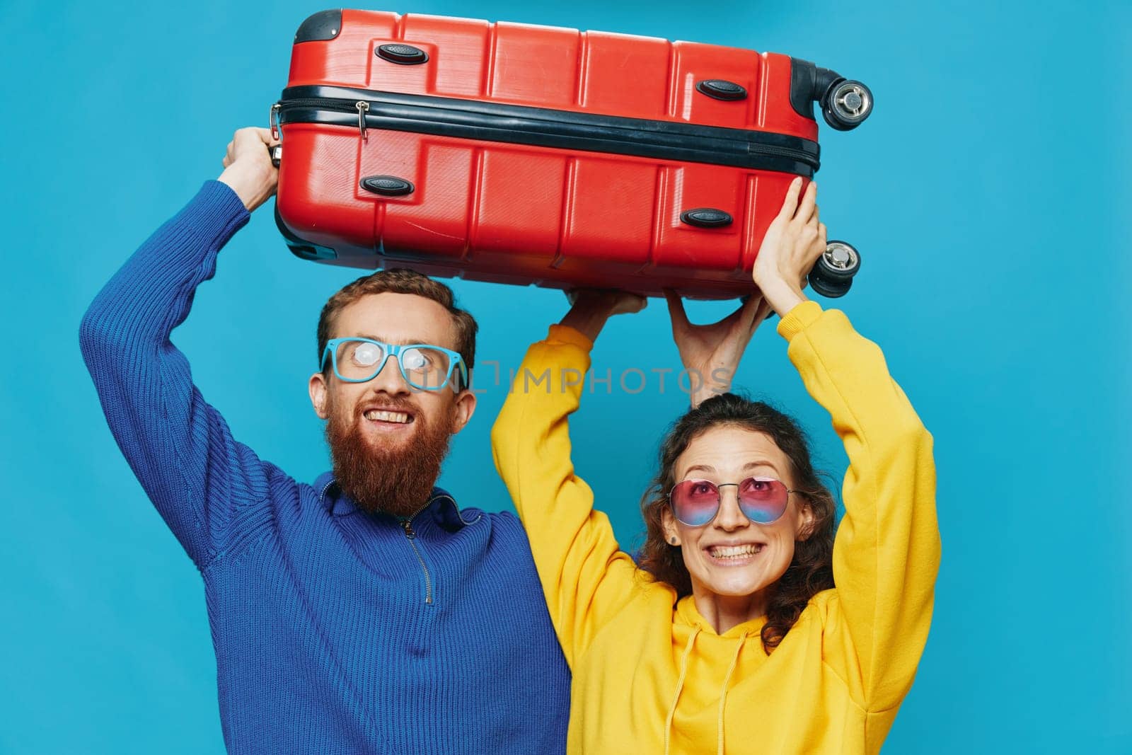 Woman and man smile suitcases in hand with yellow and red suitcase smile fun, on blue background, packing for a trip, family vacation trip. High quality photo