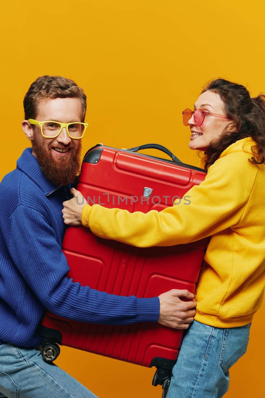 Woman and man smiling, suitcases in hand with yellow and red suitcase smiling merrily and crooked, yellow background, going on a trip, family vacation trip, newlyweds. High quality photo