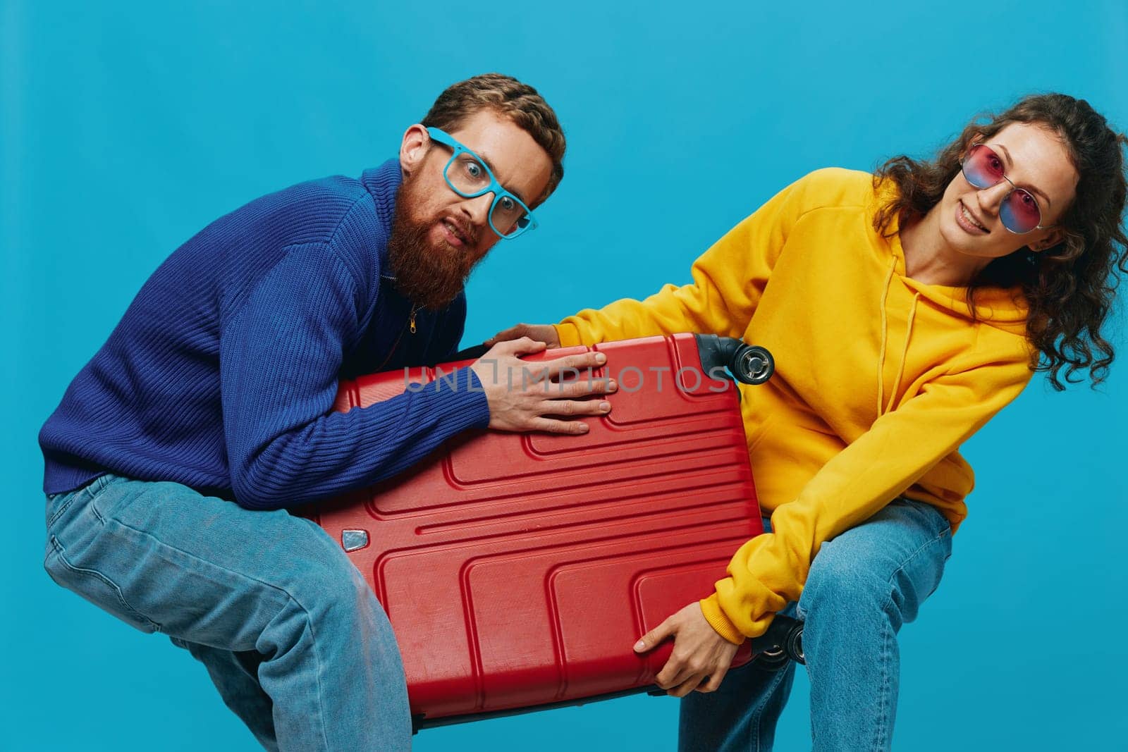 Woman and man smile suitcases in hand with yellow and red suitcase smile fun, on blue background, packing for a trip, family vacation trip. by SHOTPRIME