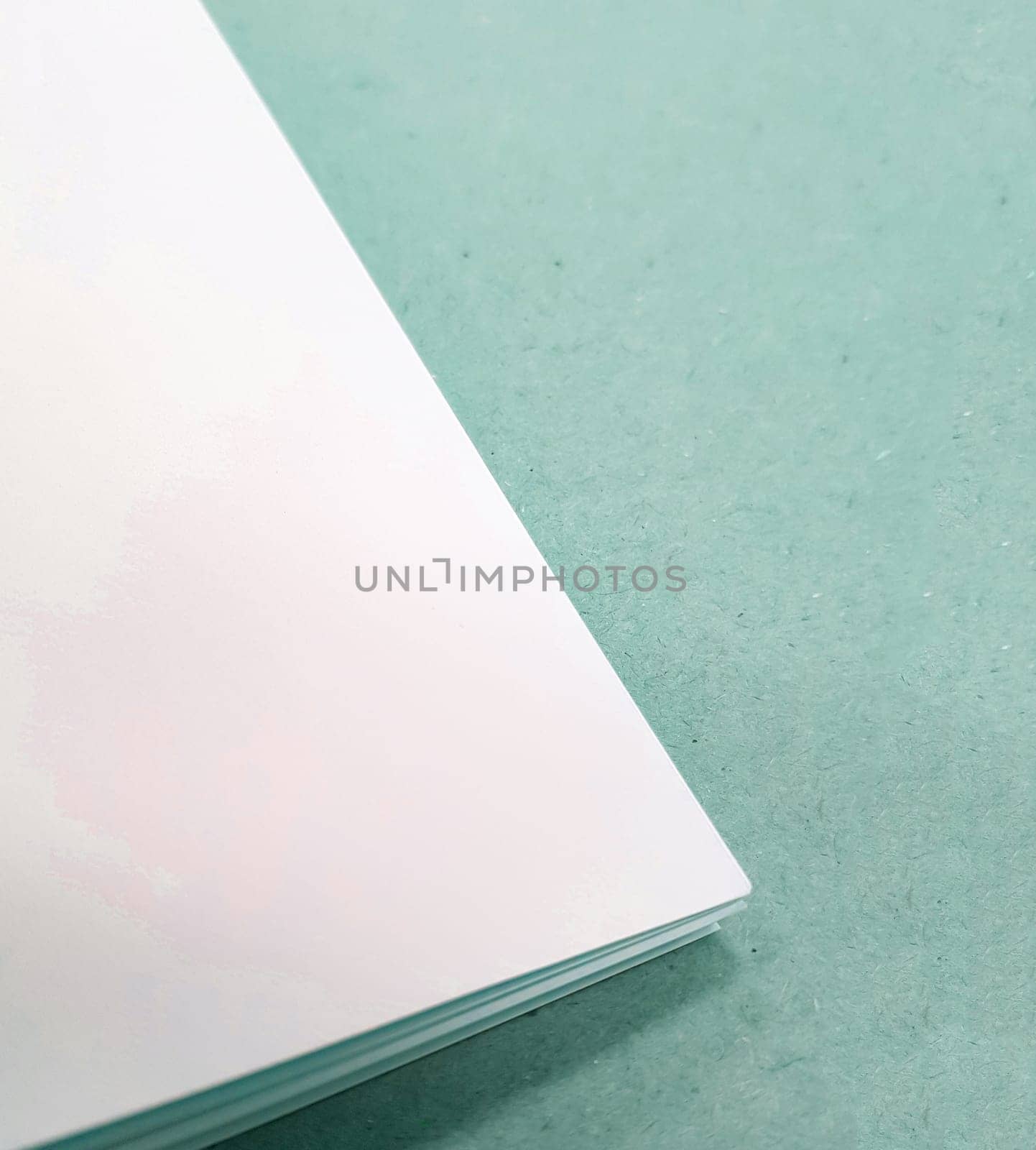 A corner of a stack of white paper sheets lies on a green background. Space for text. Top view, vertical by claire_lucia