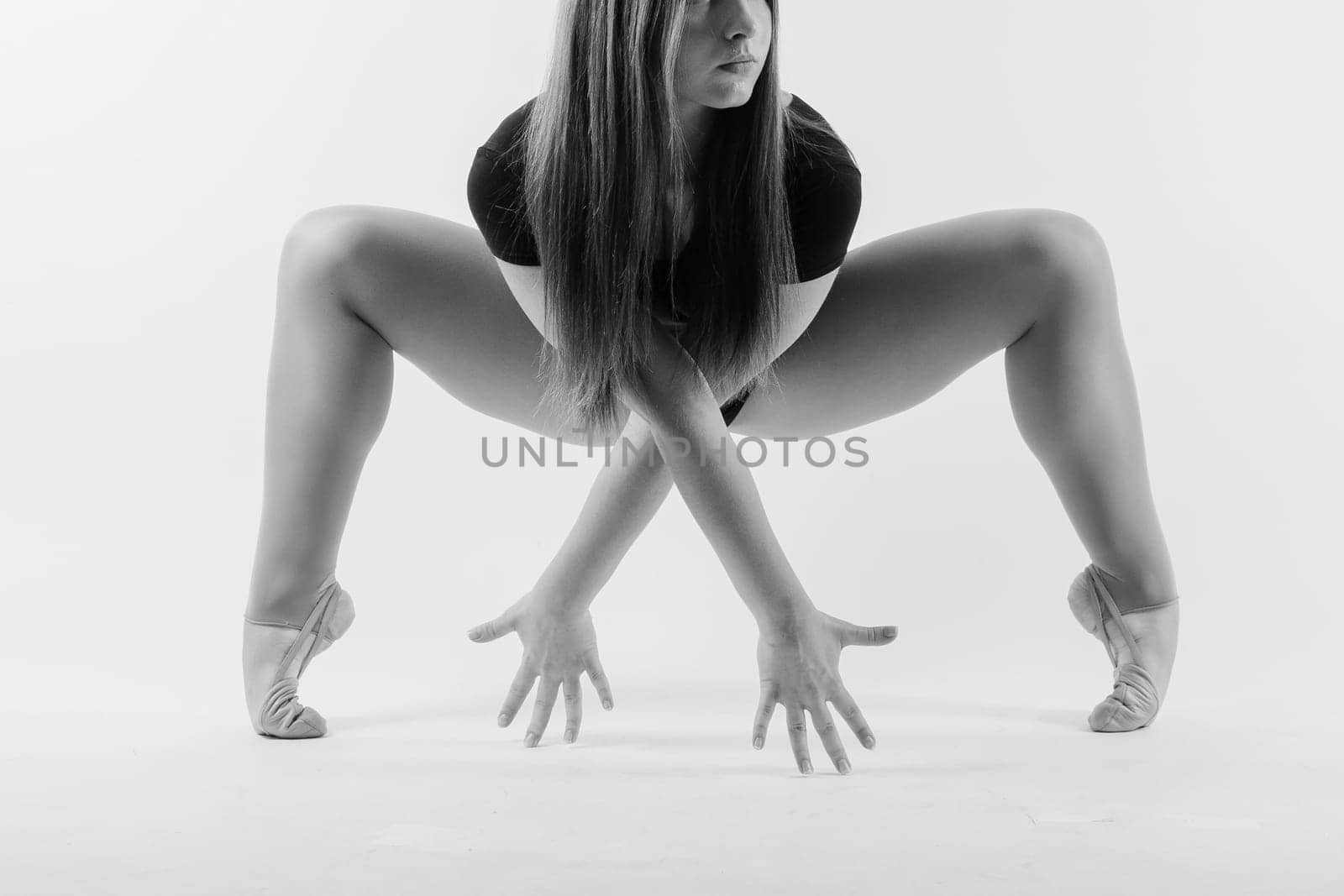 A girl gymnast in a swimsuit does tricks on white and dark background. Front view