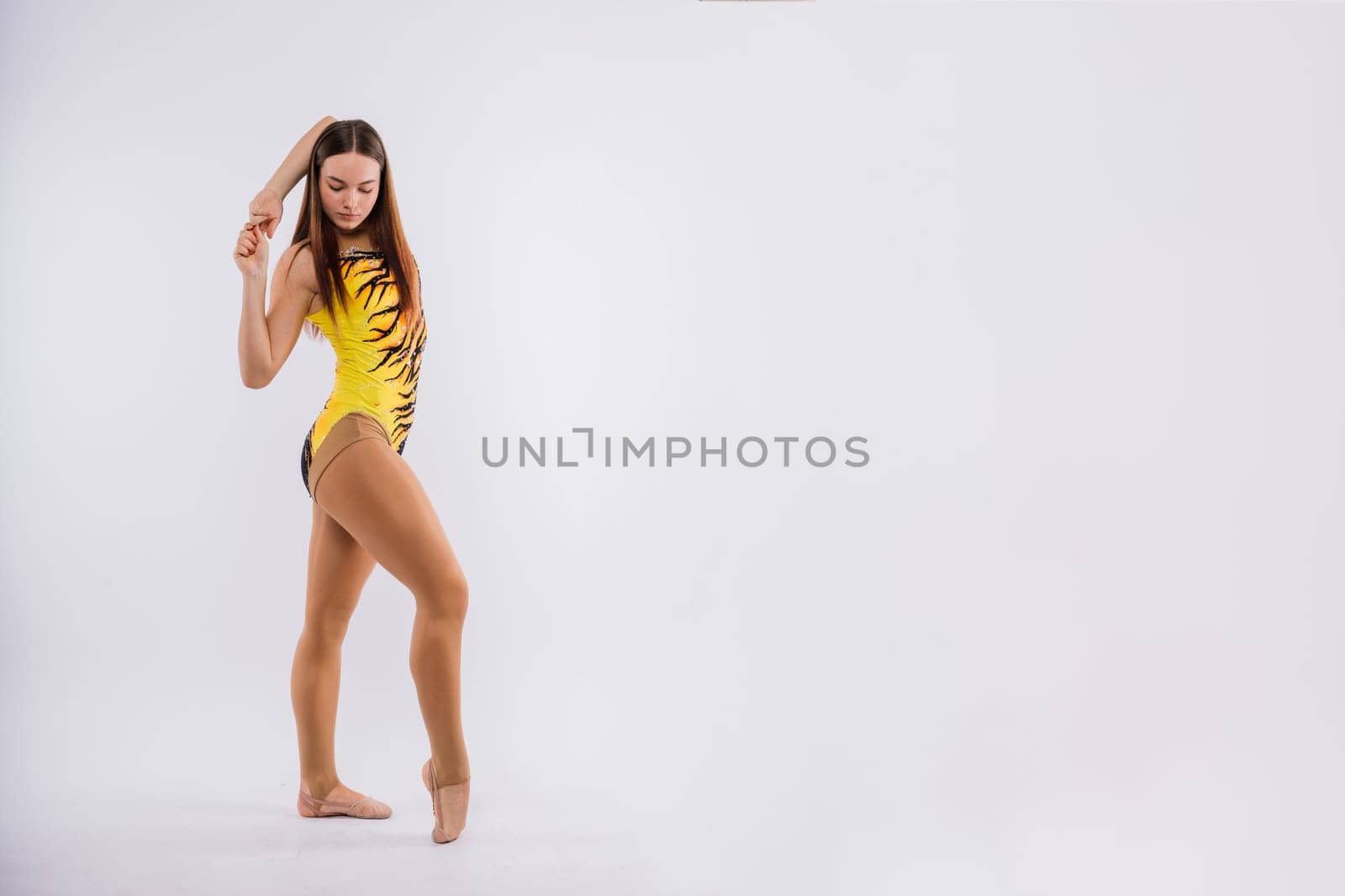 A girl gymnast in a swimsuit does tricks on white and dark background. Front view