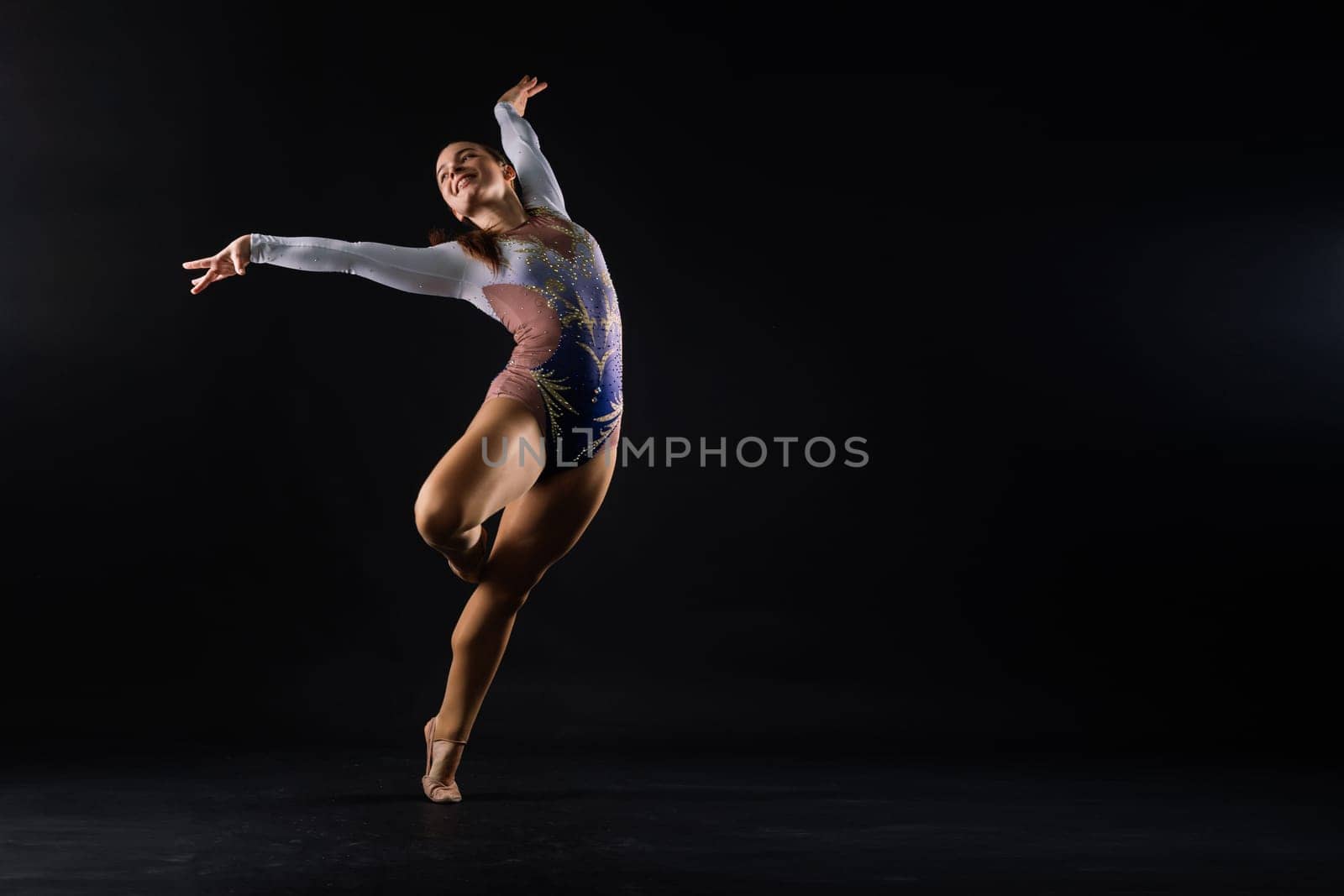 A girl gymnast in a swimsuit does tricks on white and dark background. Front view