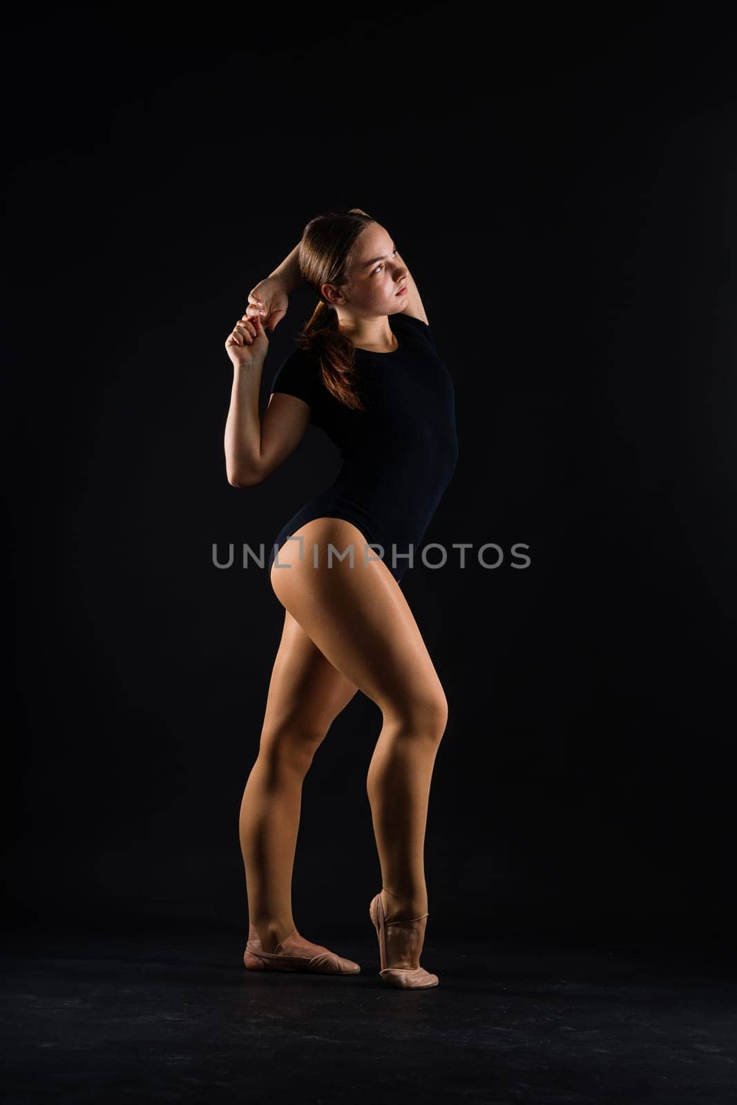 A girl gymnast in a swimsuit does tricks on white and dark background. Front view