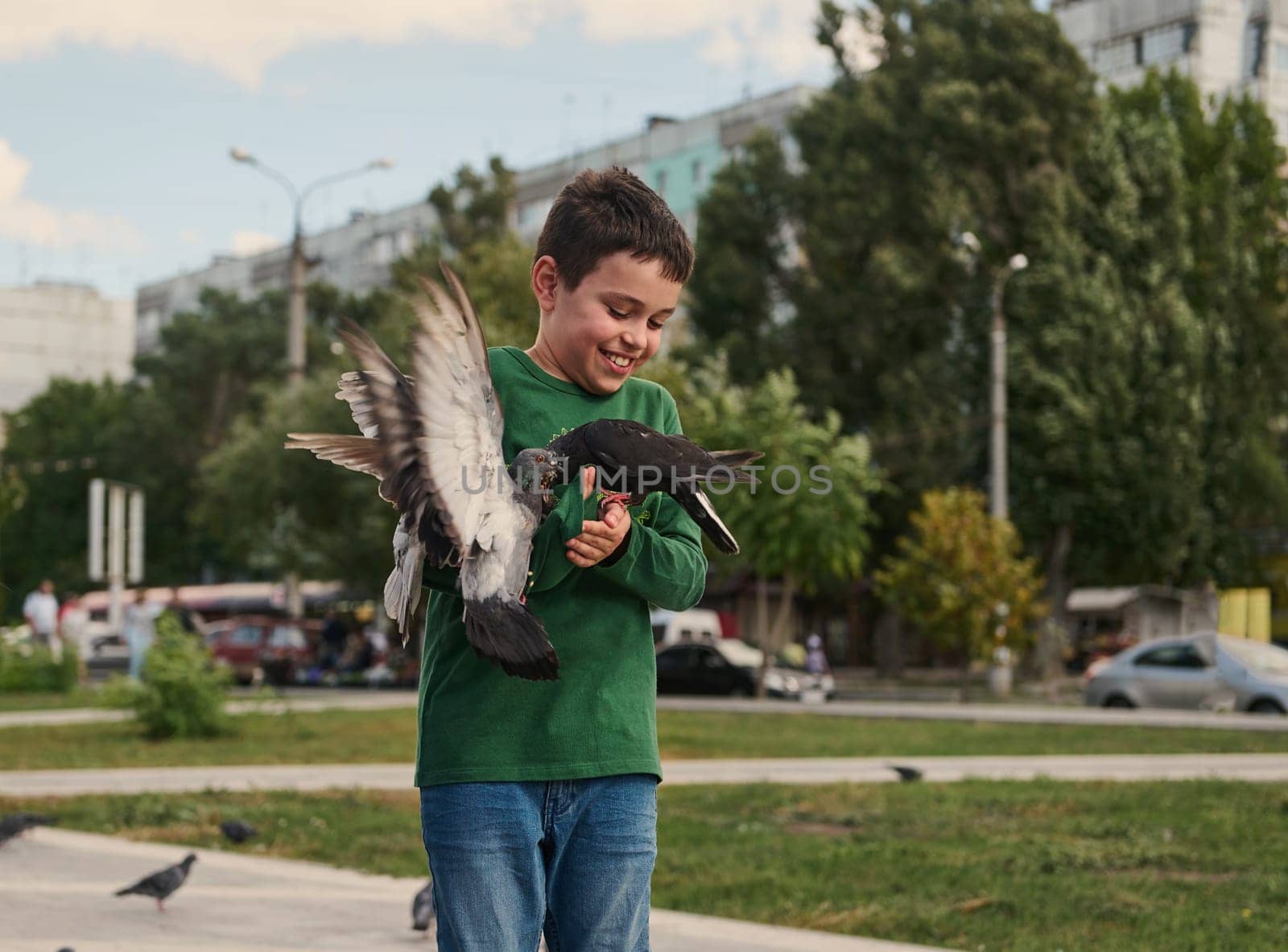 Happy positive smiling multi-ethnic teenage boy feeding pigeons on the square on a sunny spring day. The concept of love, care and compassion for wild animals. People. Nature. Lifestyle