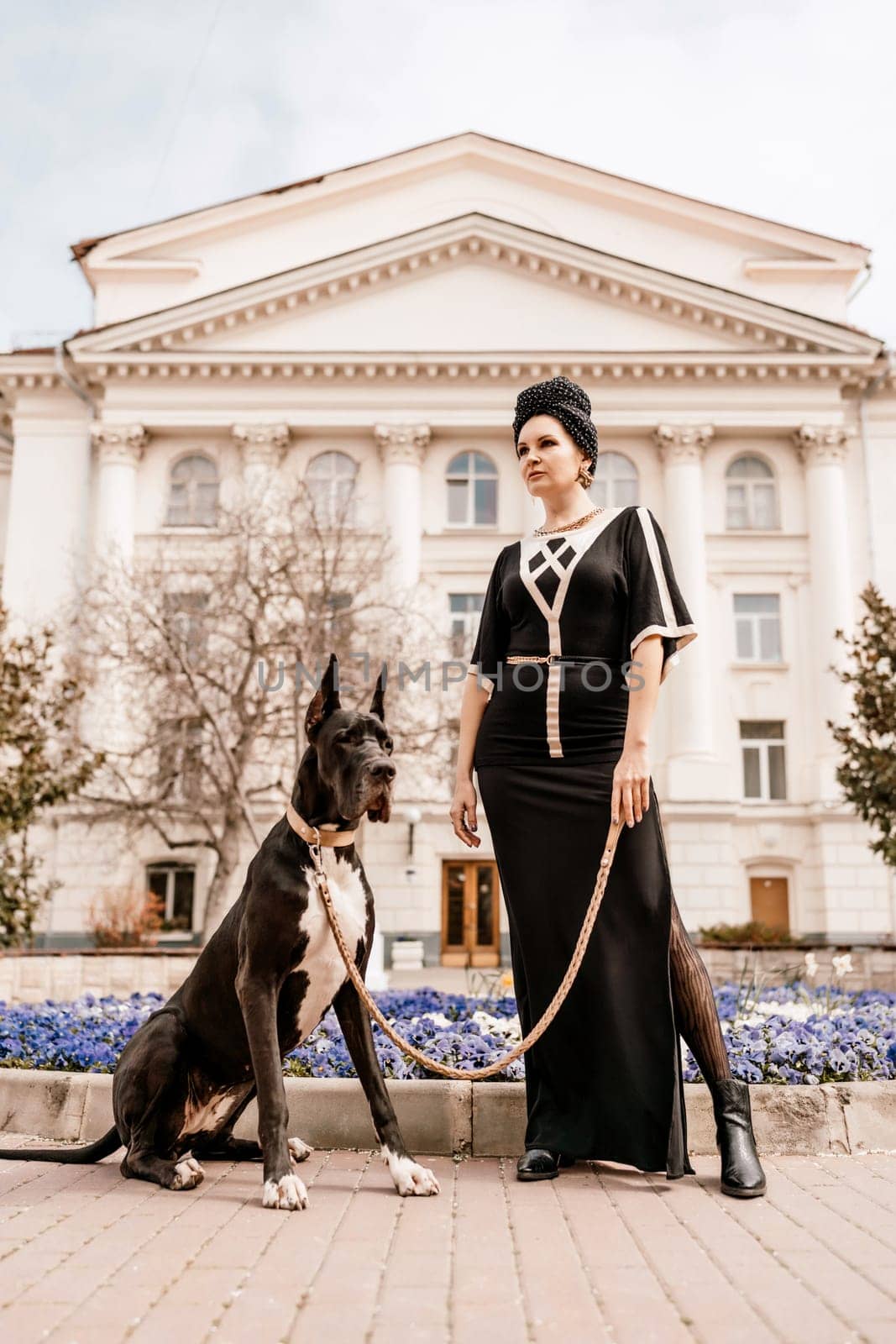 A photo of a woman and her Great Dane walking through a town, taking in the sights and sounds of the urban environment.