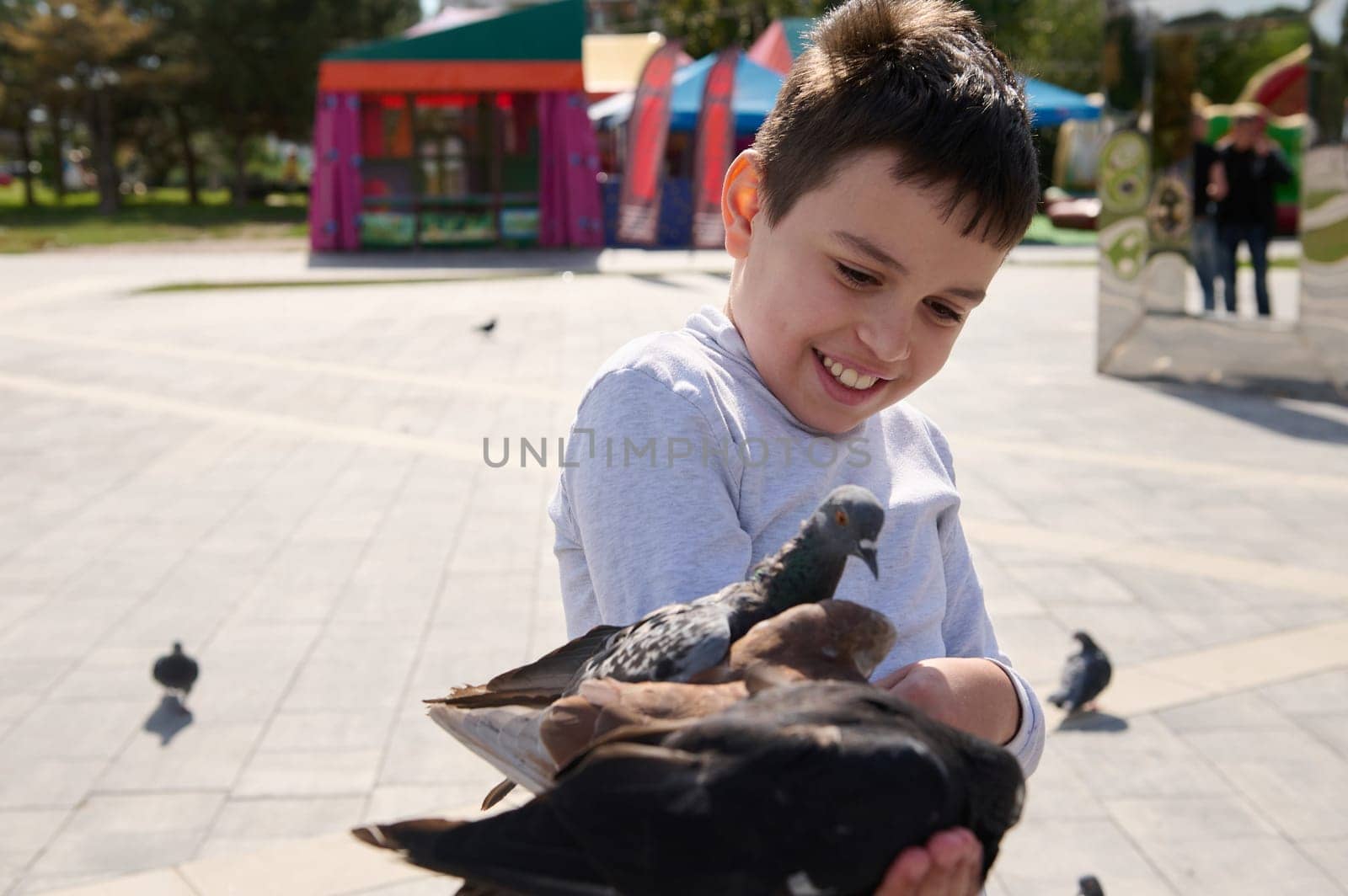 Friendly joyful kid boy feeds pigeons in city summer park. The concept of kindness and care for animals. Happy childhood by artgf