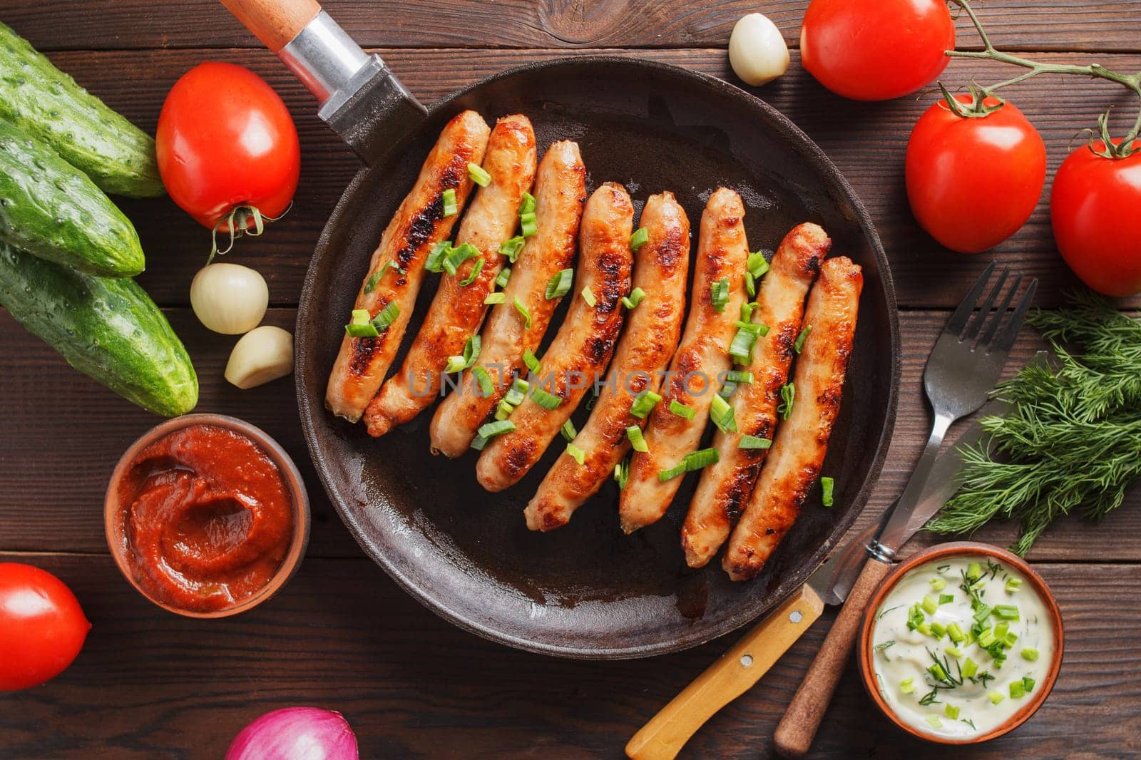 Delicious sausages cooked in a pan with vegetables and various sauces on a wooden table.