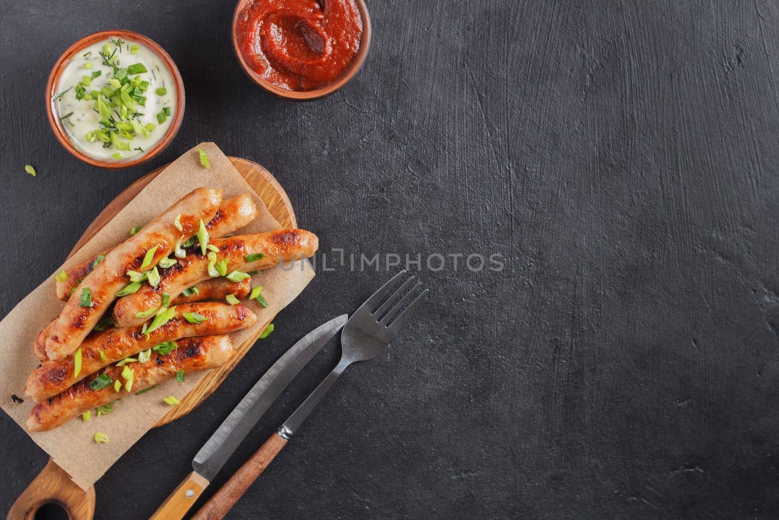 Delicious sausages on a wooden board with various sauces on a black background. copy space. by lara29