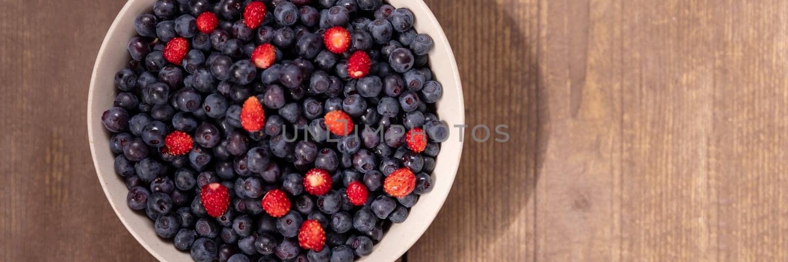 Strawberries and blueberries arranged in a heart shaped bowl on a rustic wooden table.