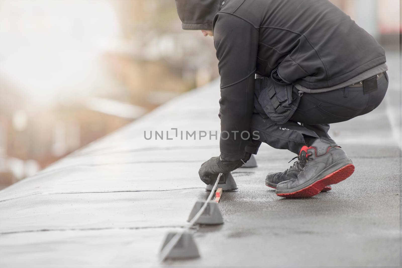 Ground wire. A worker lays a ground cable on the roof of a building. Electrician fixing aluminum wire for grounding solar panels.