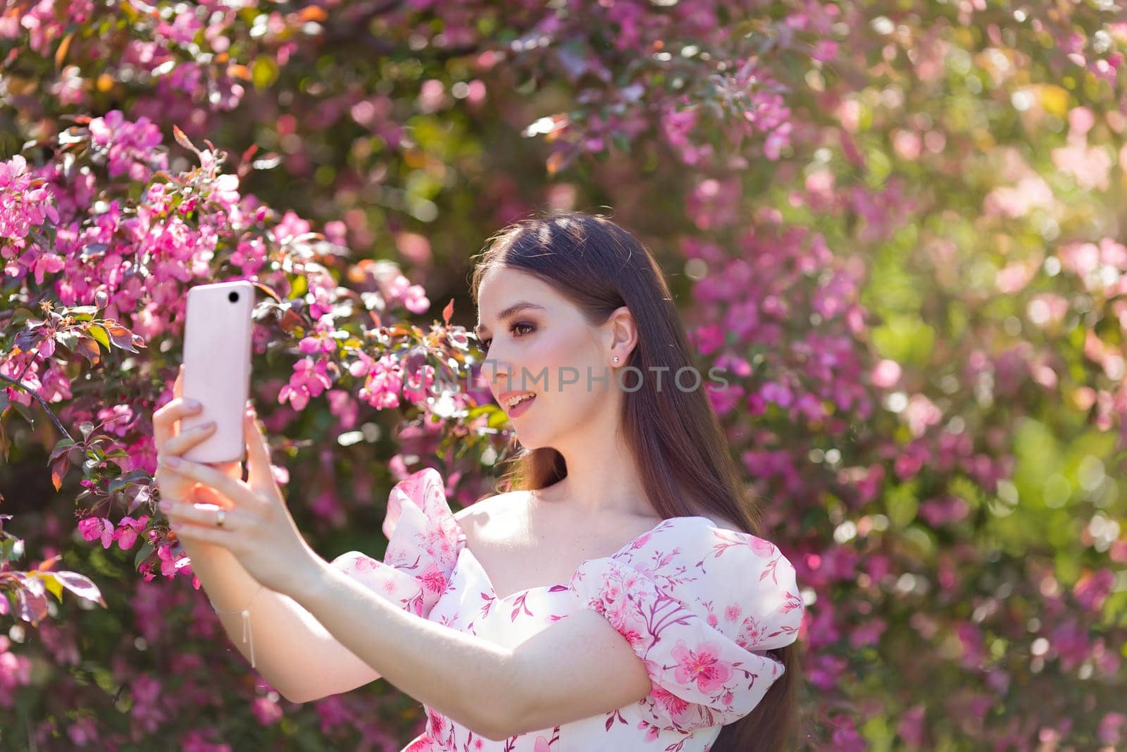 girl is standing near a pink blooming apple tree with smartphone by Zakharova