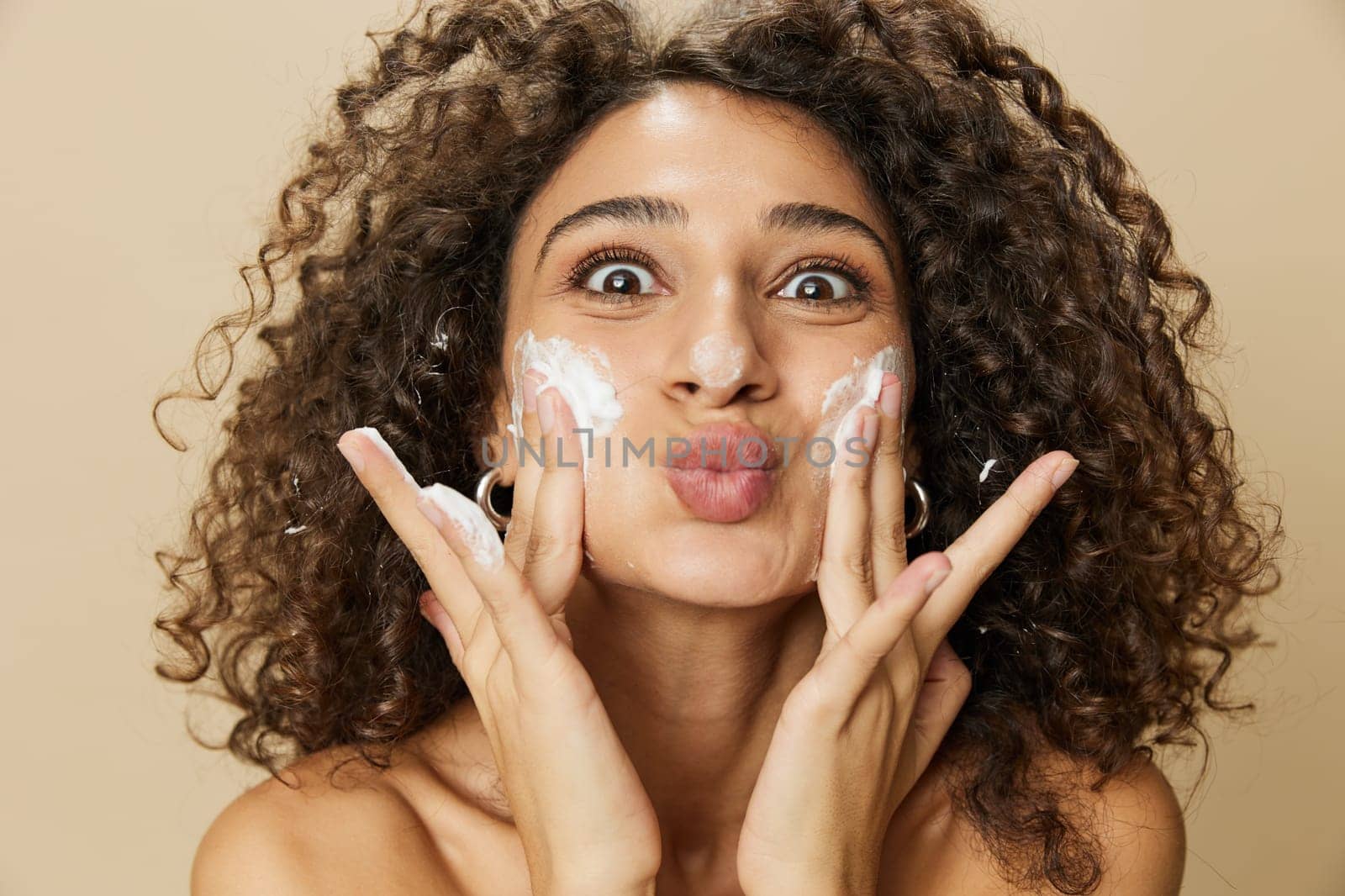 Woman beauty face close-up applying foam to wash and cleanse skin with fingers of her hand, nail and hair health, hair dryer style curly afro hair, body and beauty care concept. High quality photo