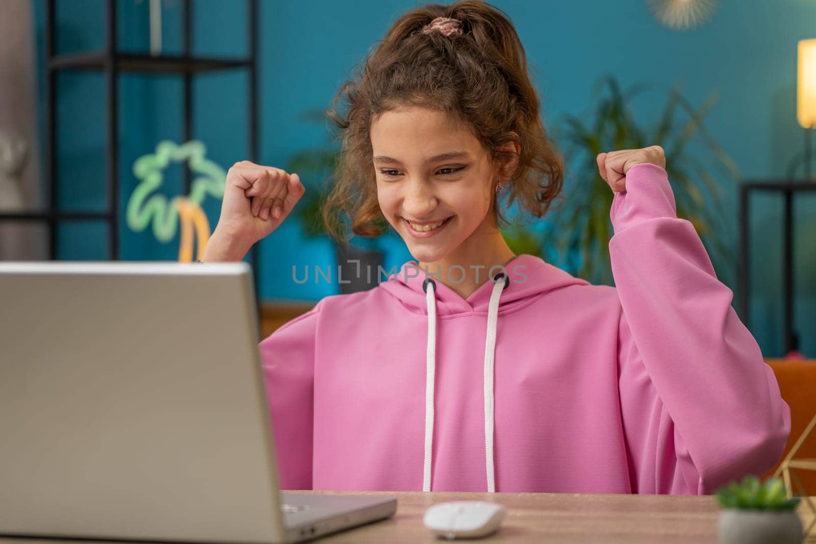 Excited caucasian preteen school girl use laptop celebrate success win triumph victory, positive test, exam results. Happy young child, kid get online good news at home workplace sitting at the table