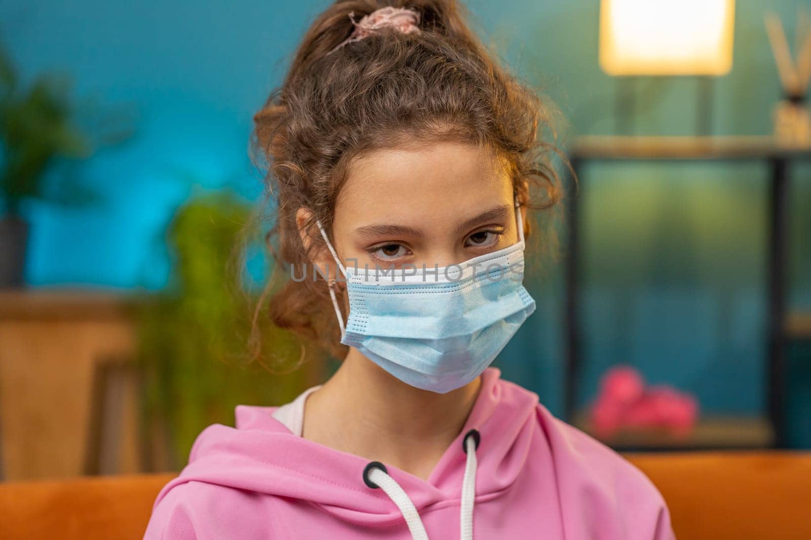 Sick preteen school girl in medical protective face mask looking to camera. Young ill child kid at home room apartment. Concept of quarantine, pandemic, pneumonia, allergy. Prevention virus diseases