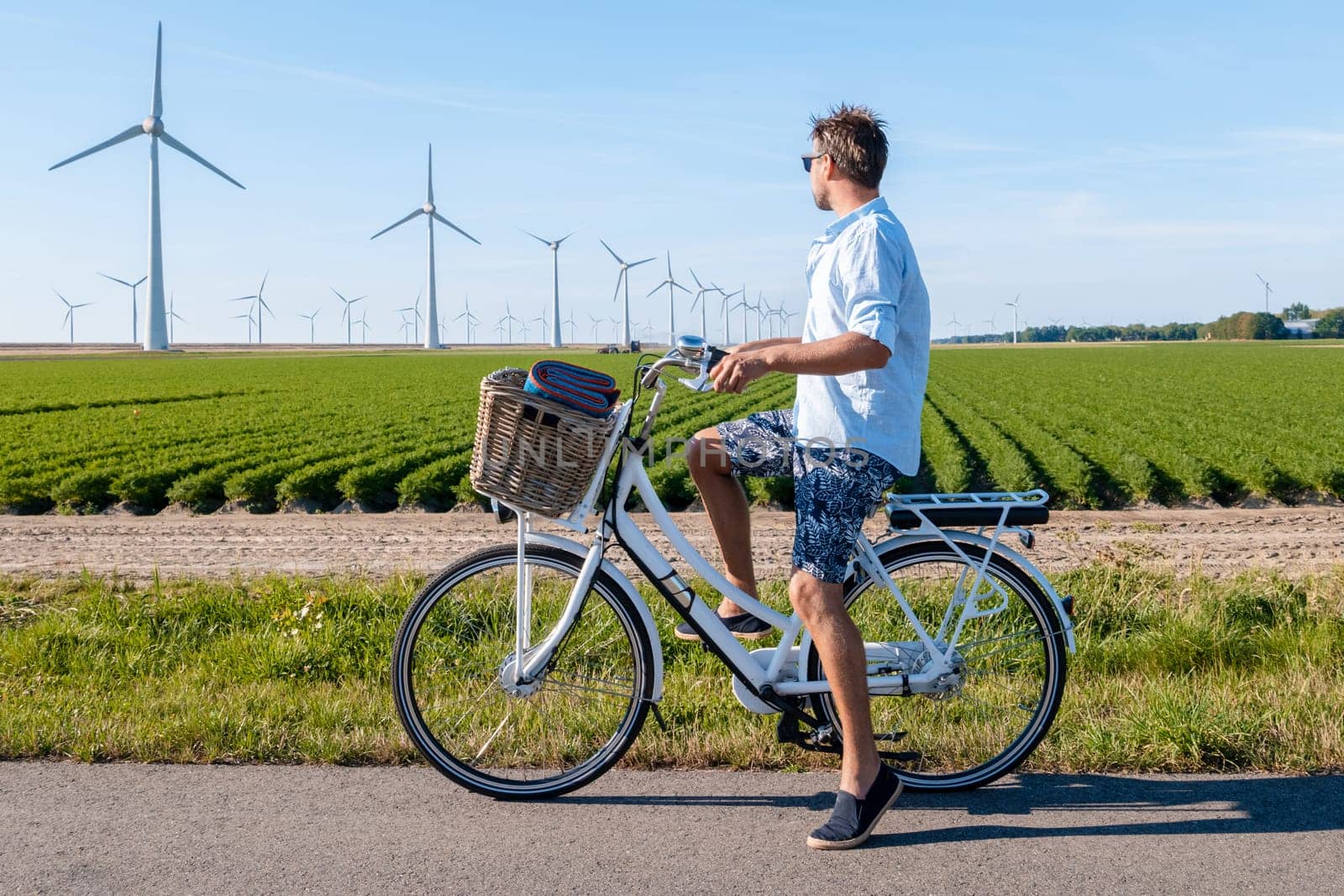young man electric green bike bicycle by windmill farm , windmills isolated on a beautiful summer by fokkebok
