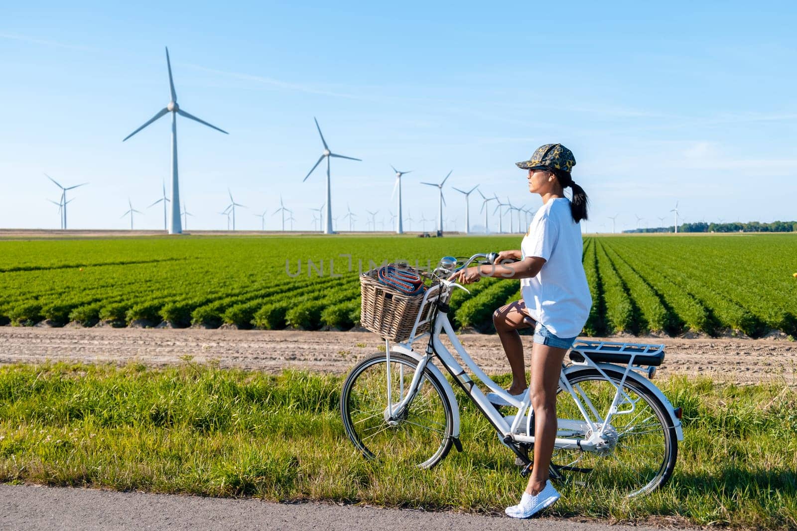 young woman electric green bike bicycle by a windmill farm with a green agricultural field, windmills isolated on a beautiful bright day in Netherlands Flevoland Noordoostpolder