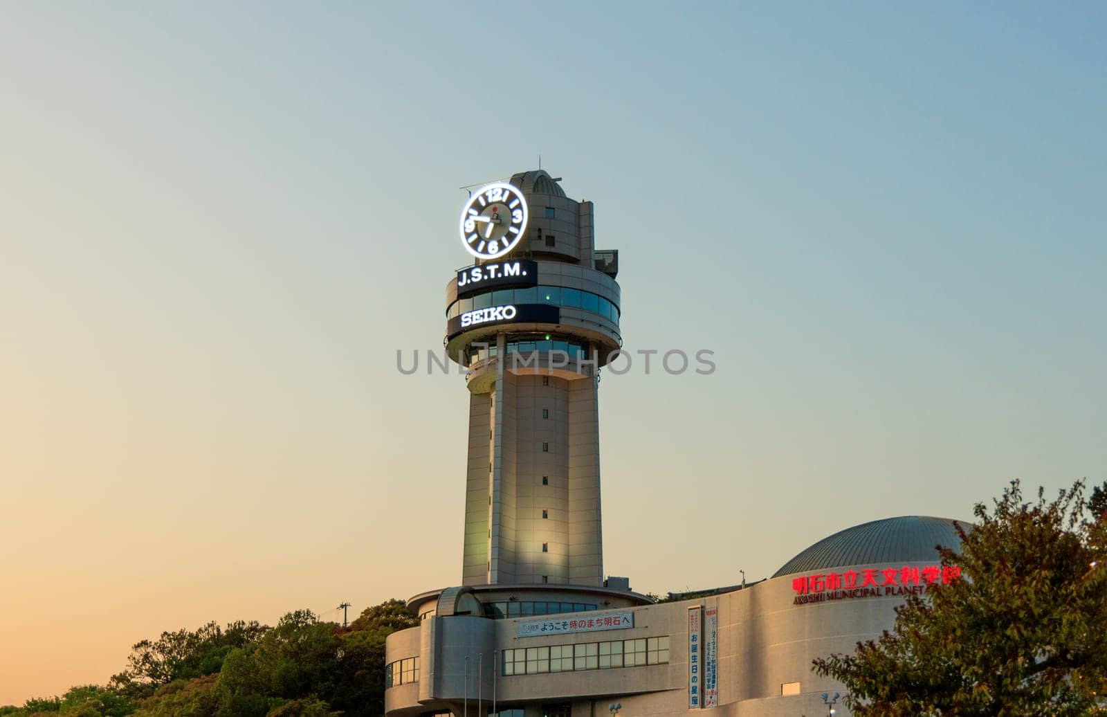 Akashi, Japan - April 19, 2023: Clock tower above planetarium with sunset color in sky by Osaze