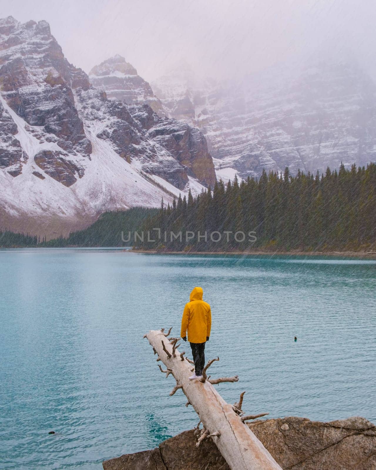 Lake Moraine during a cold snowy day in Autumn in Canada, Beautiful turquoise waters of the Moraine Lake with snow. couple of men and women in yellow raincoat jackets during snow