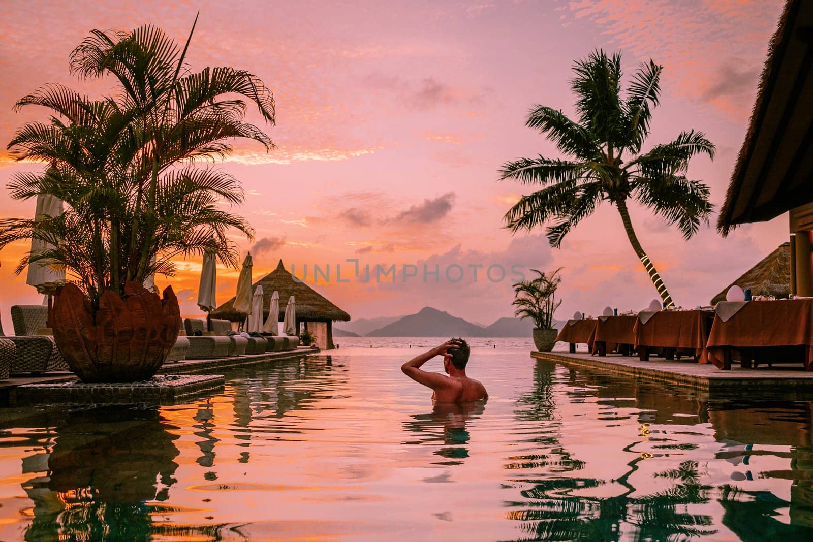 young men in swimming pool during sunset, Luxury swimming pool in tropical resort by fokkebok