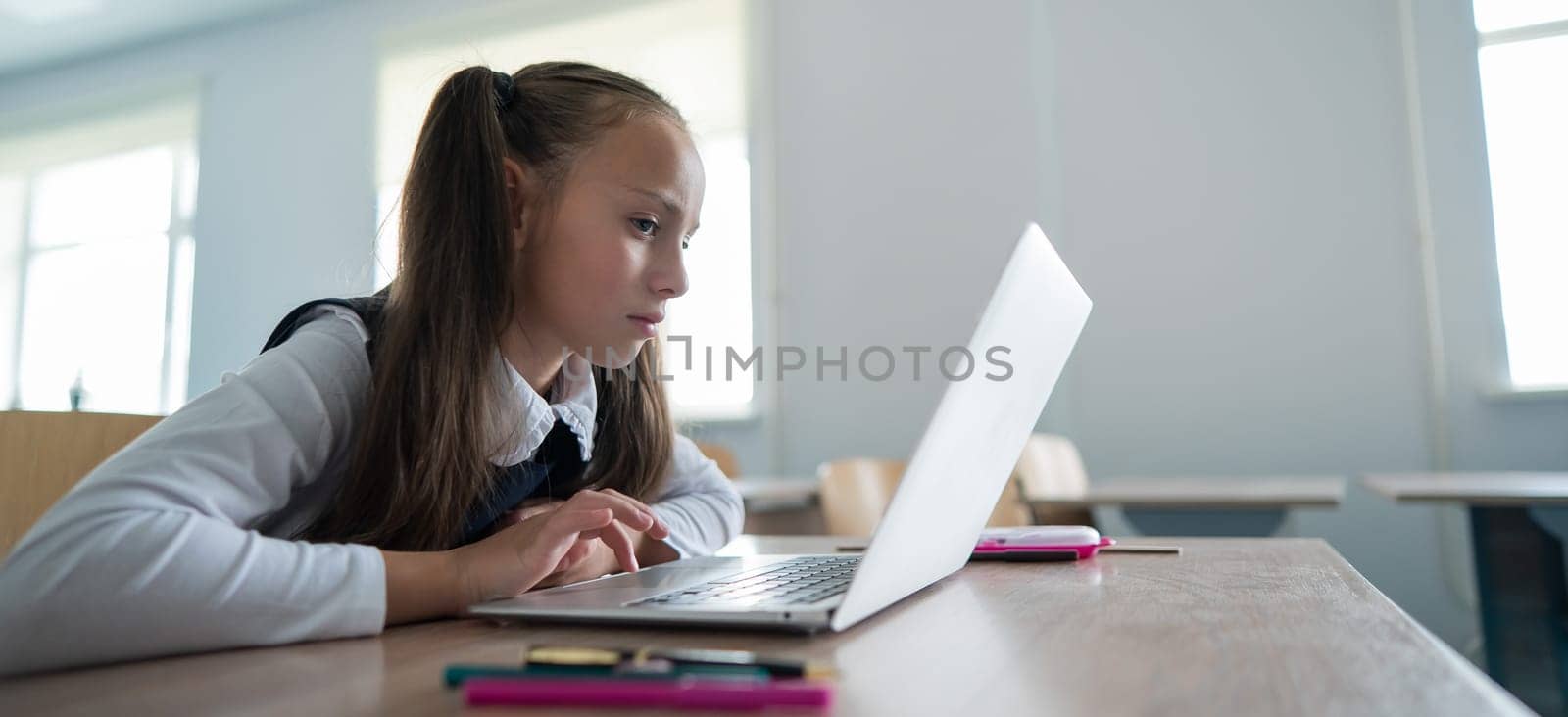 Caucasian girl sits at a desk at school and carefully looks into a laptop. by mrwed54