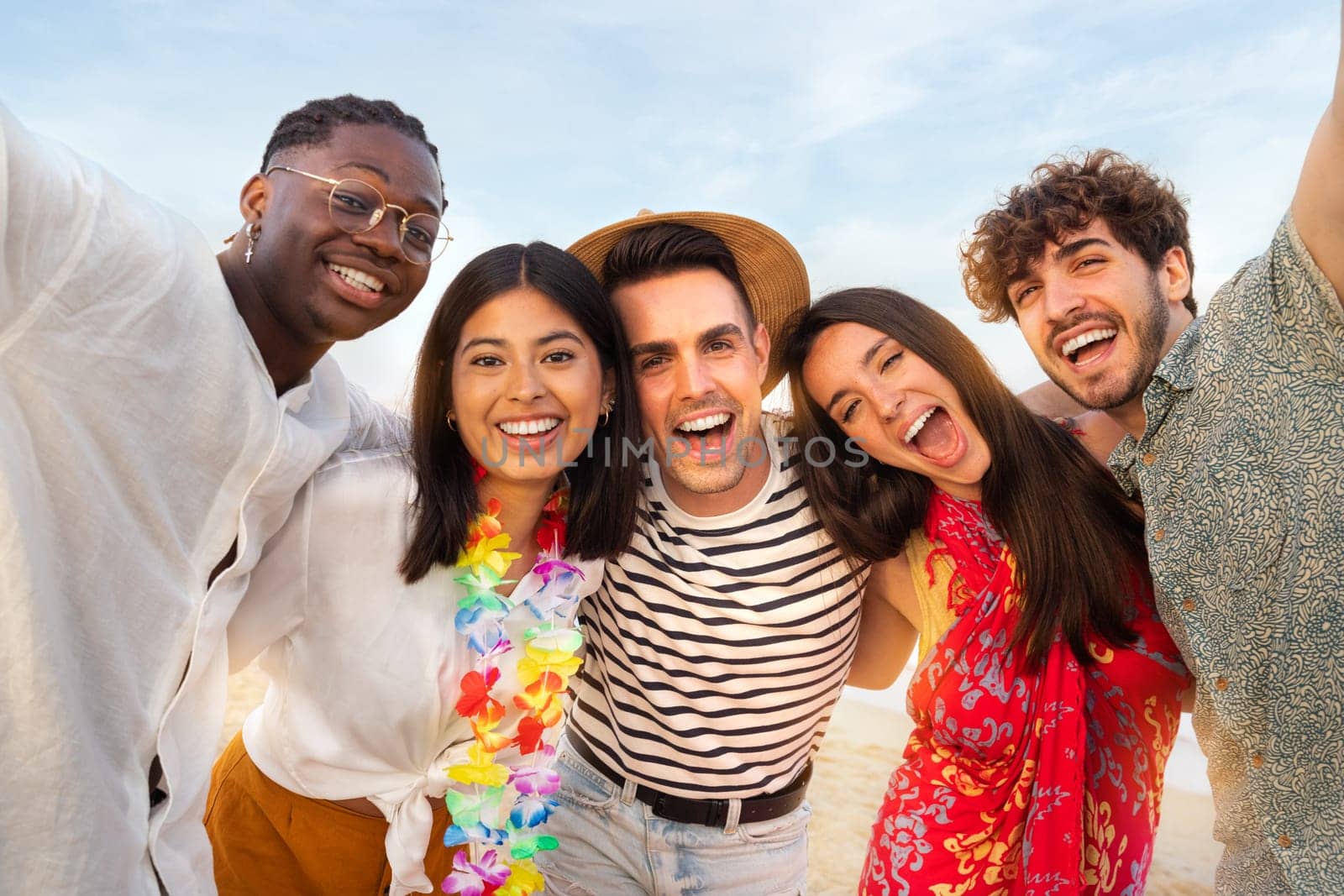 Happy, smiling group of multiracial friends relaxing at the beach having fun together looking at camera. Summer vacation and friendship concept.